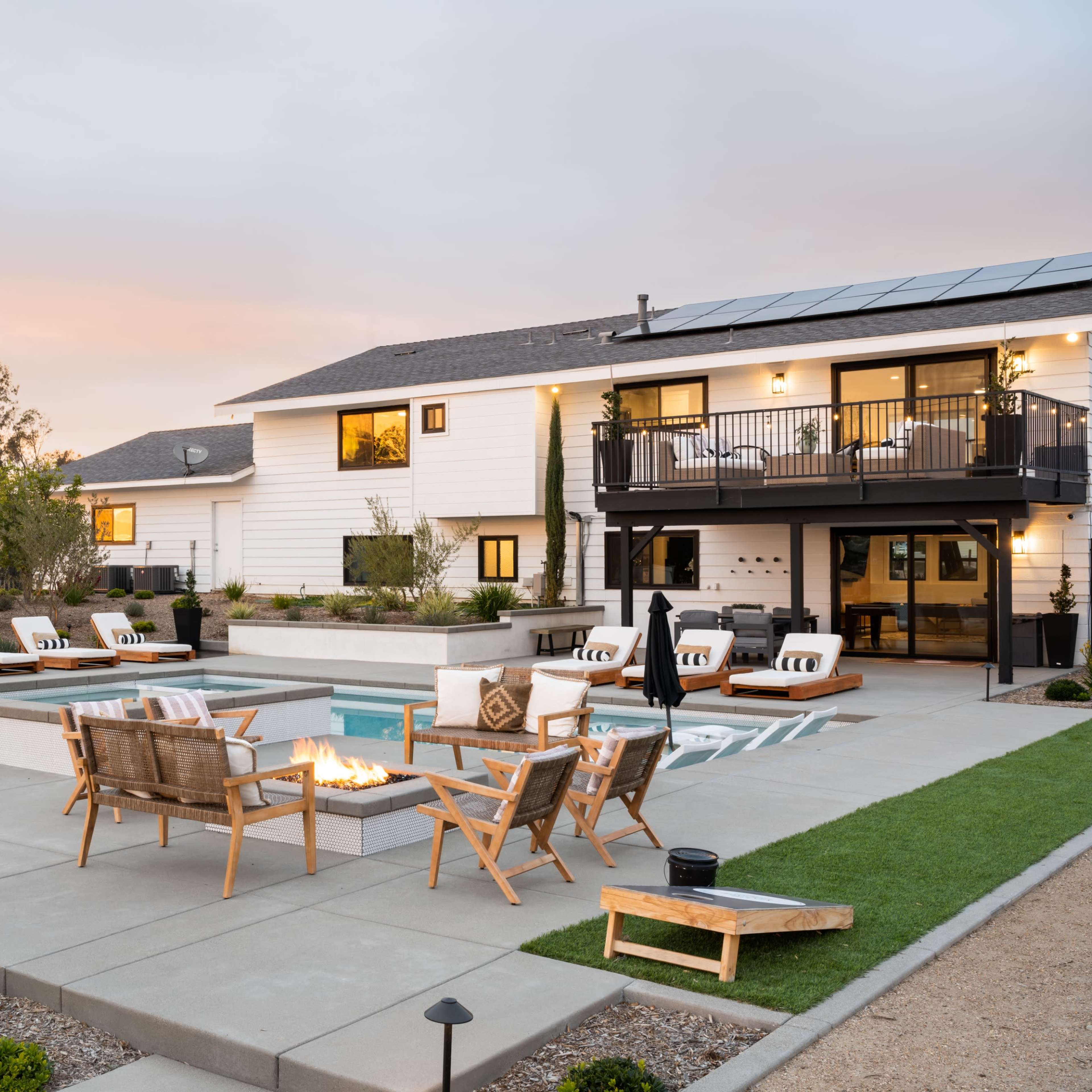 A modern backyard with a swimming pool, fire pit, and outdoor seating arranged around a concrete patio next to a two-story house.