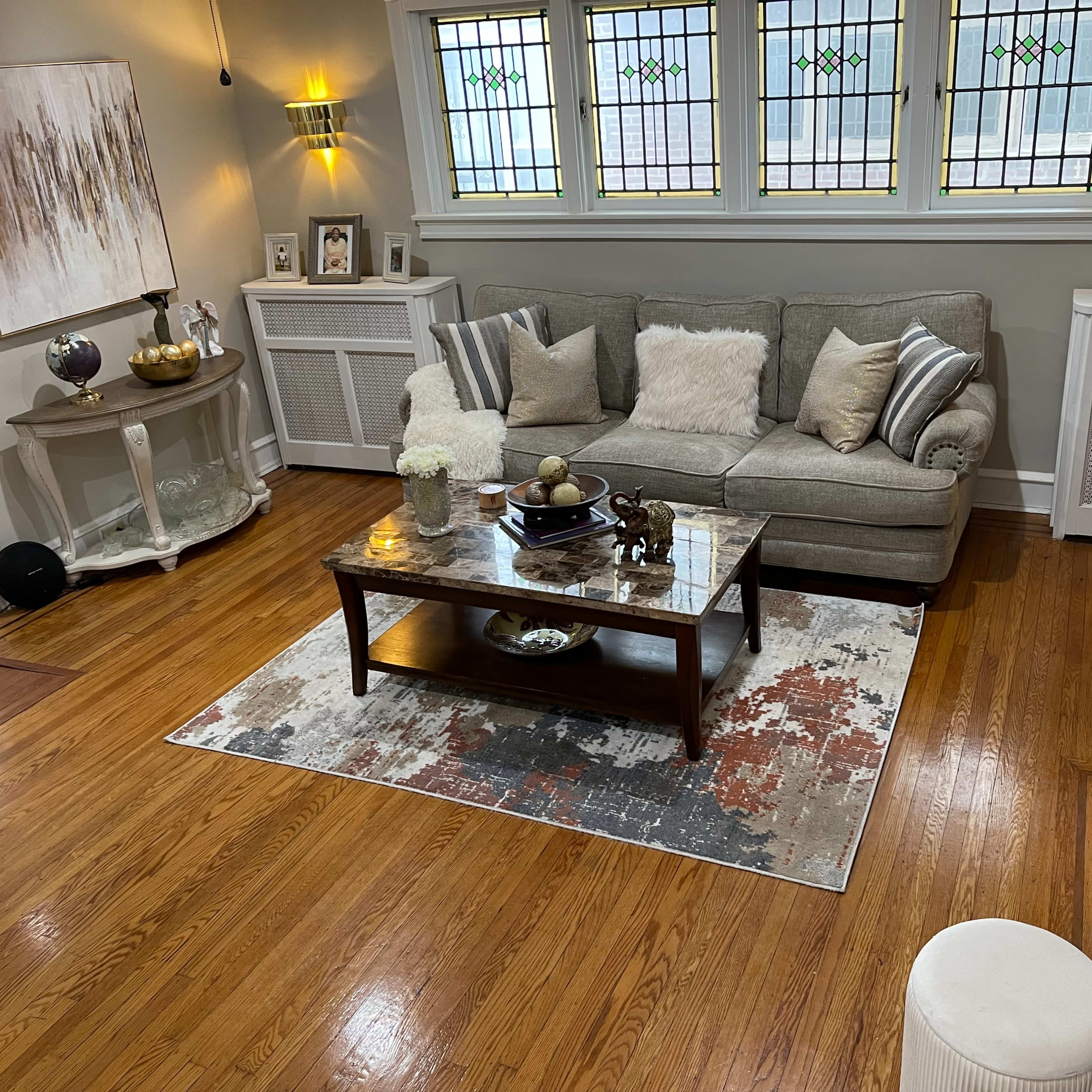 A cozy living room with a gray sofa, a wooden coffee table on a patterned area rug, and various decorative items on a side table and shelves.