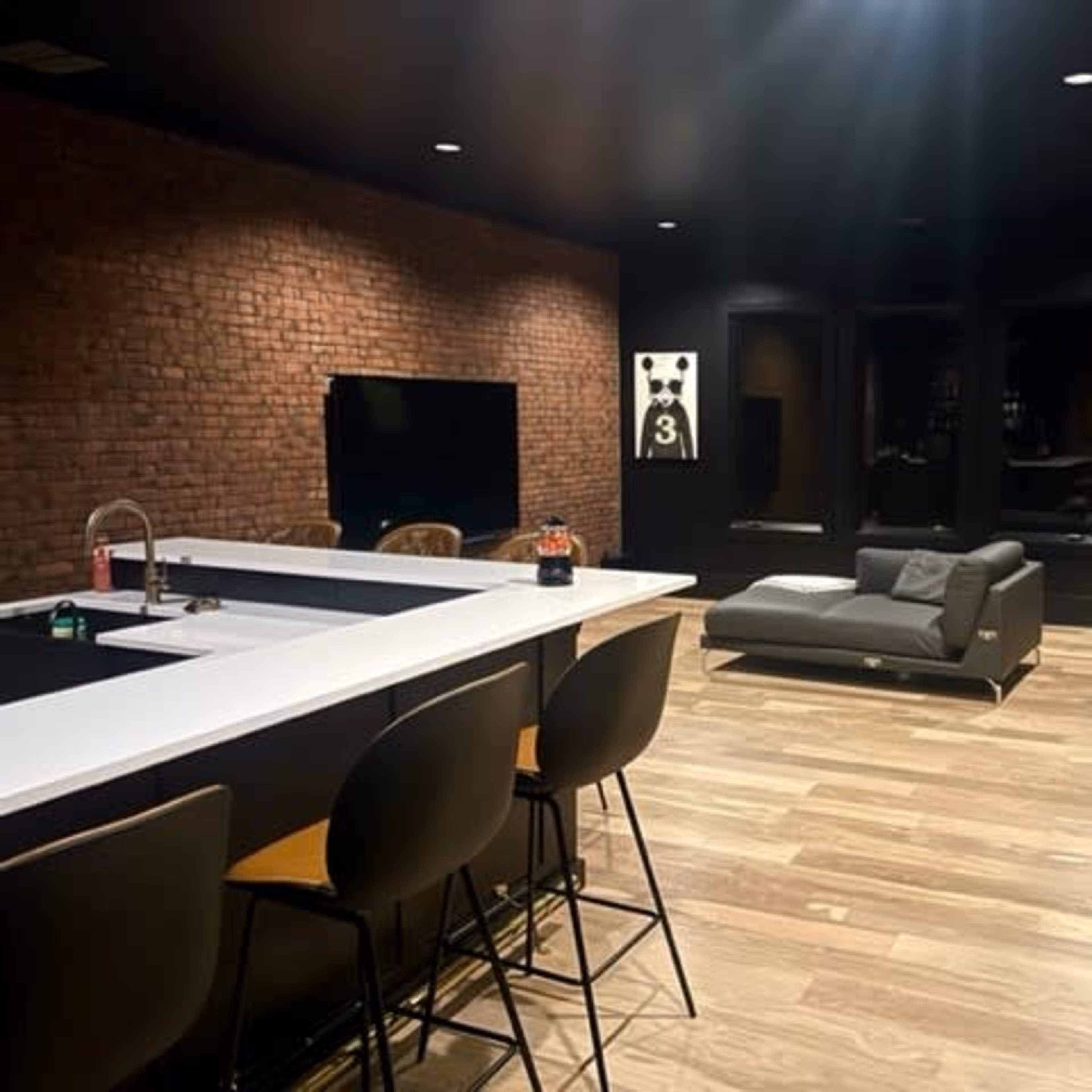 A modern indoor space featuring a sleek kitchen bar with high chairs, a brick wall, and a sectional sofa beside framed artwork.