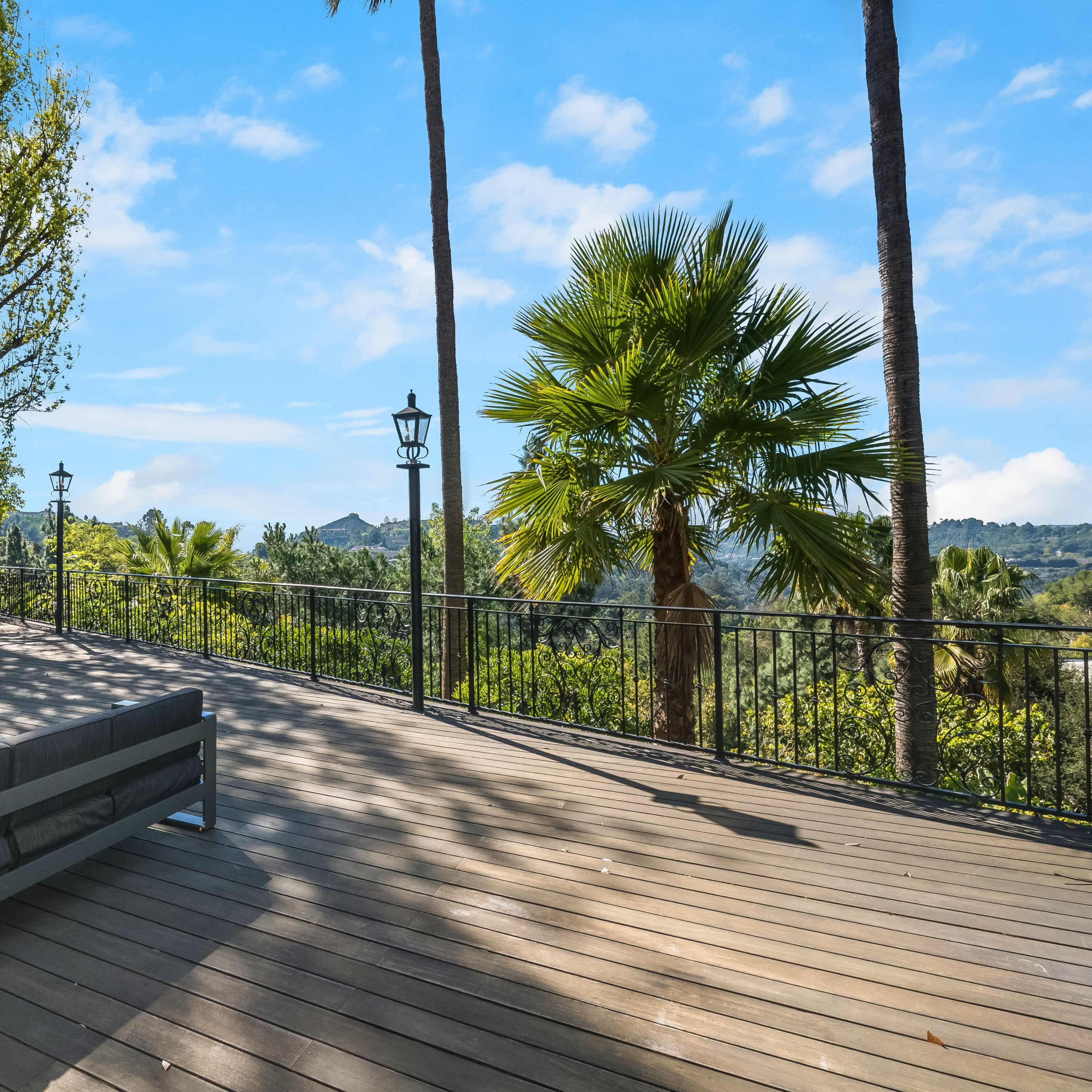 A wooden deck with modern seating, surrounded by palm trees and lush greenery under a clear blue sky.