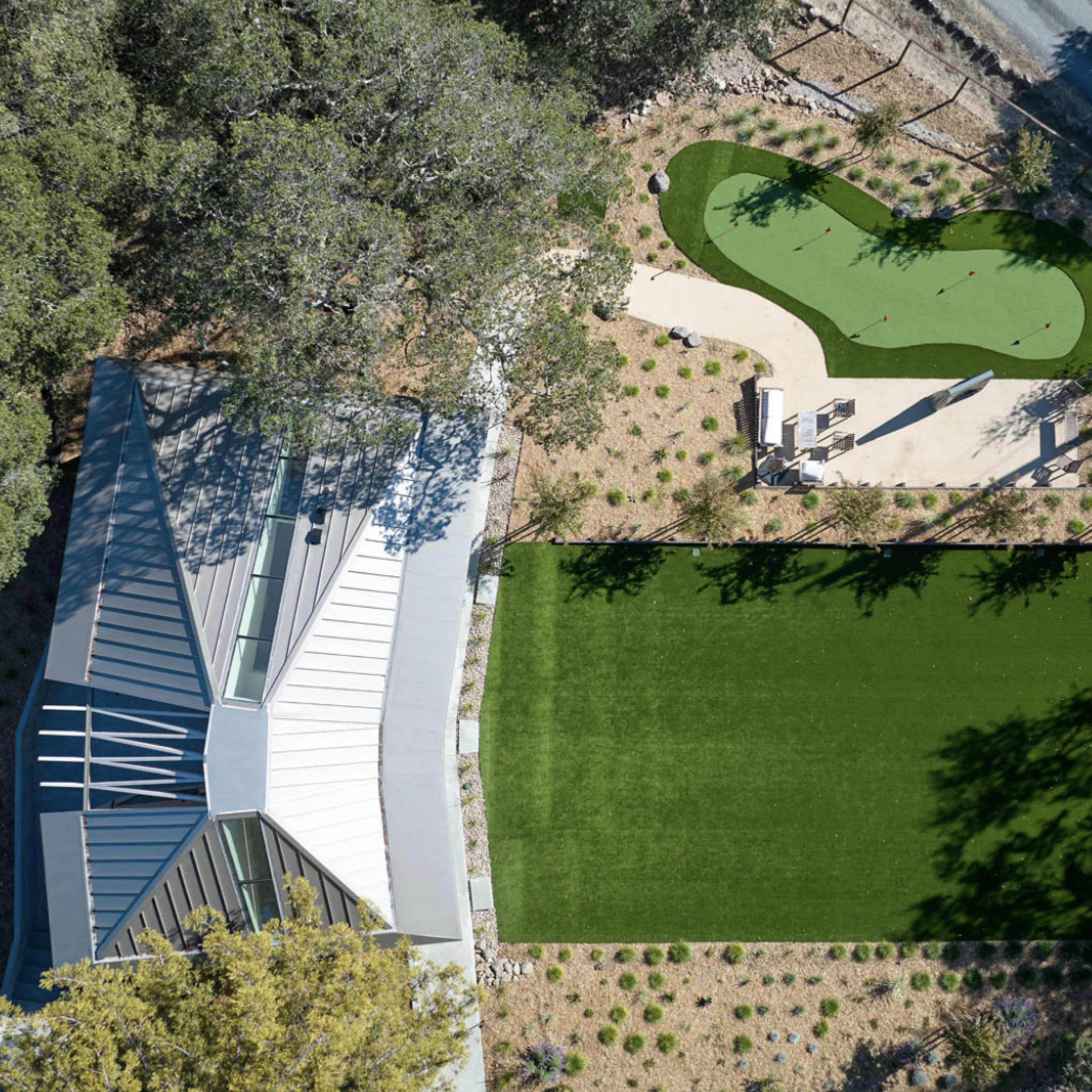 An aerial view of a modern house surrounded by landscaped areas, featuring a green lawn and a small putting green.