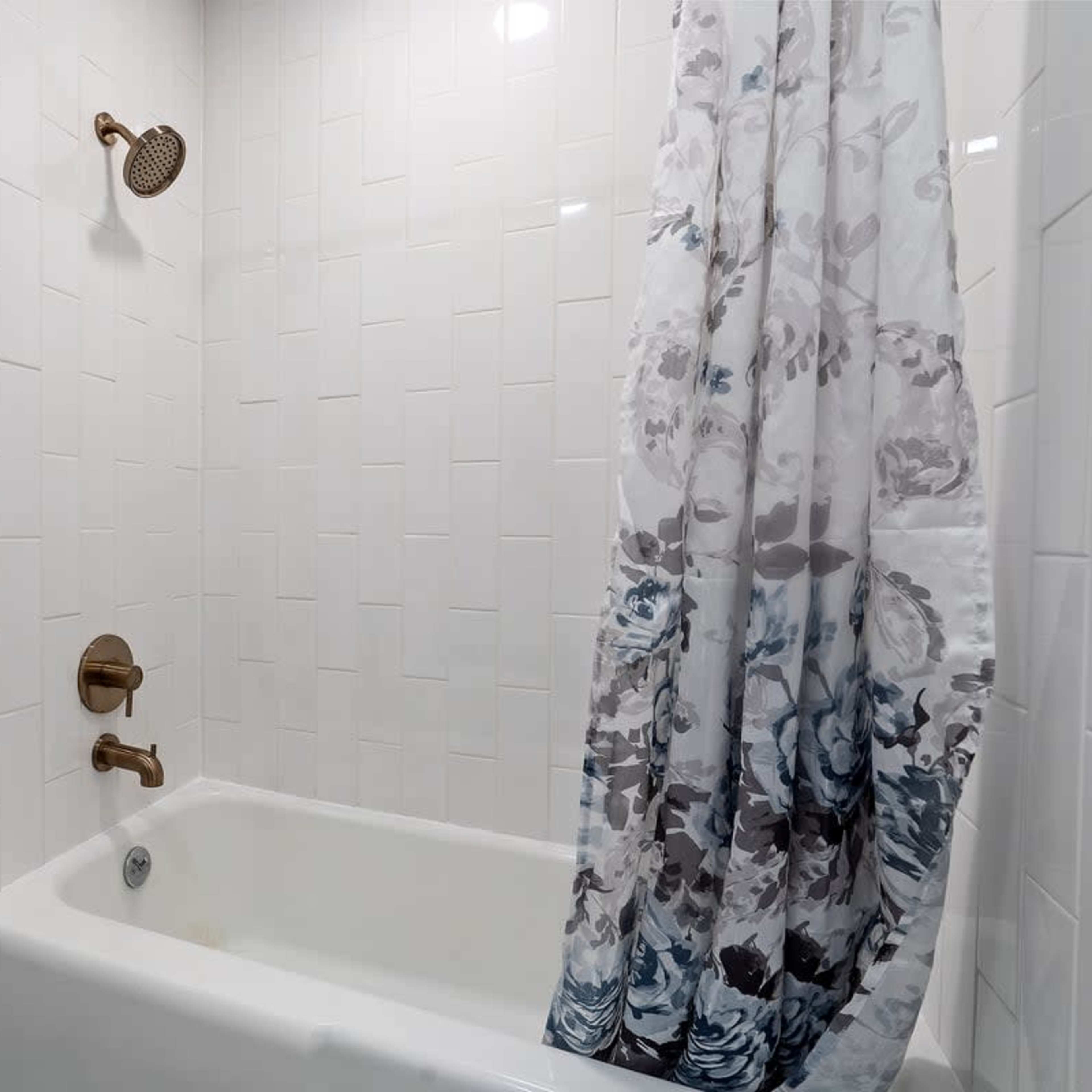 A bathroom with a white bathtub, a shower head mounted on the wall, and a floral-patterned shower curtain.