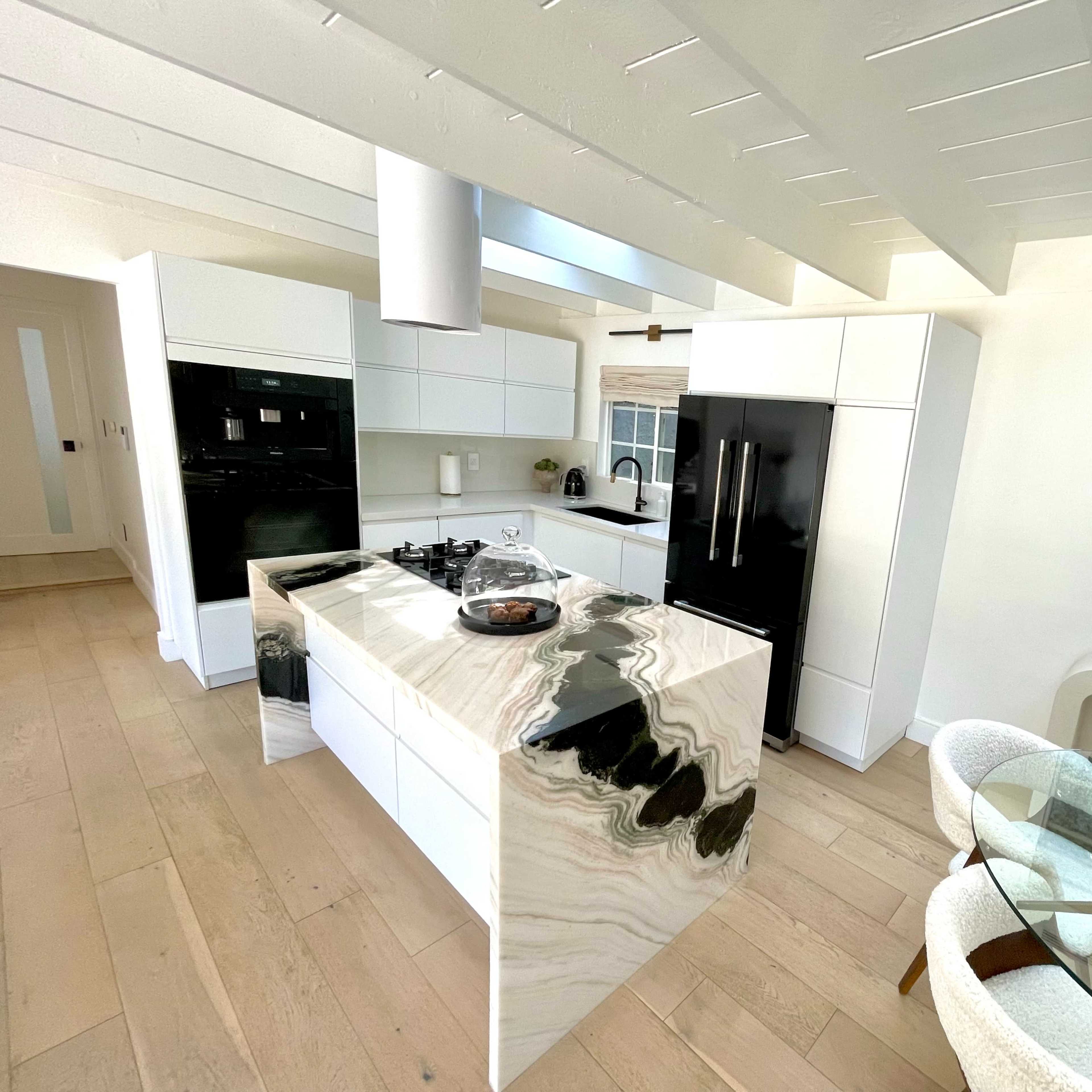 A modern kitchen featuring a marble island, black and white cabinetry, and a dining area with a circular table.