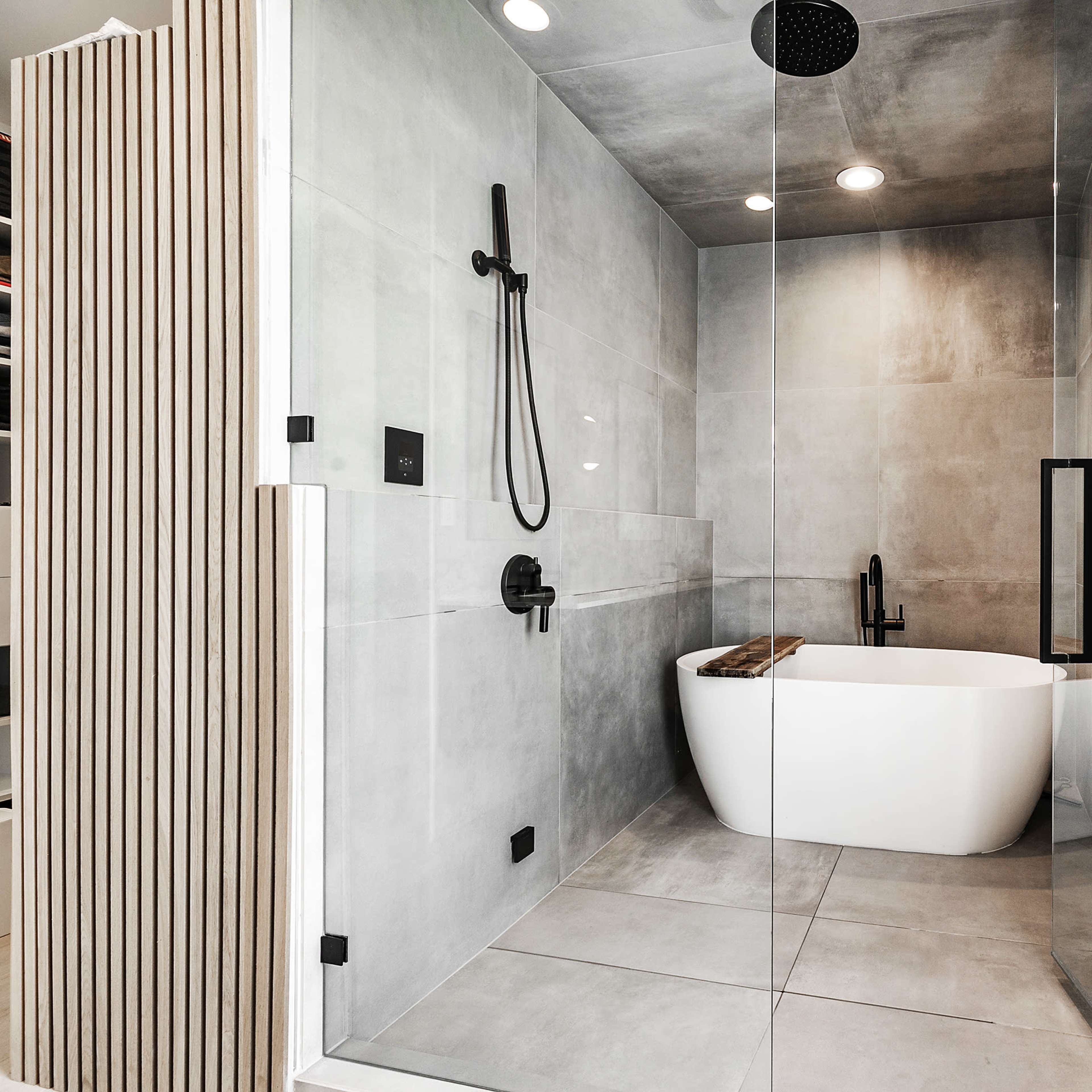 A modern bathroom featuring a glass shower enclosure, a freestanding bathtub, and sleek gray tile walls.
