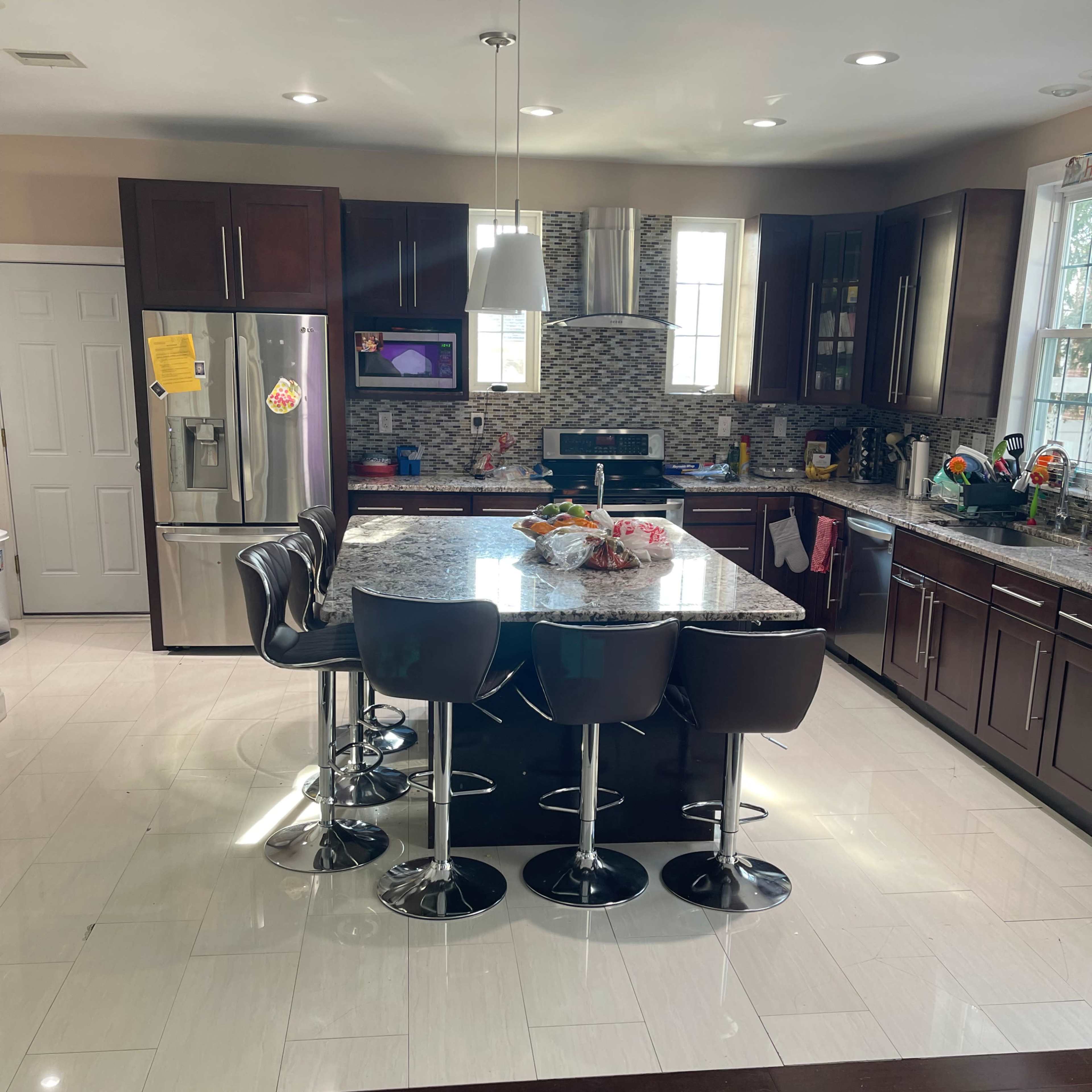 A modern kitchen with dark cabinetry, a large granite island with bar stools, and stainless steel appliances.