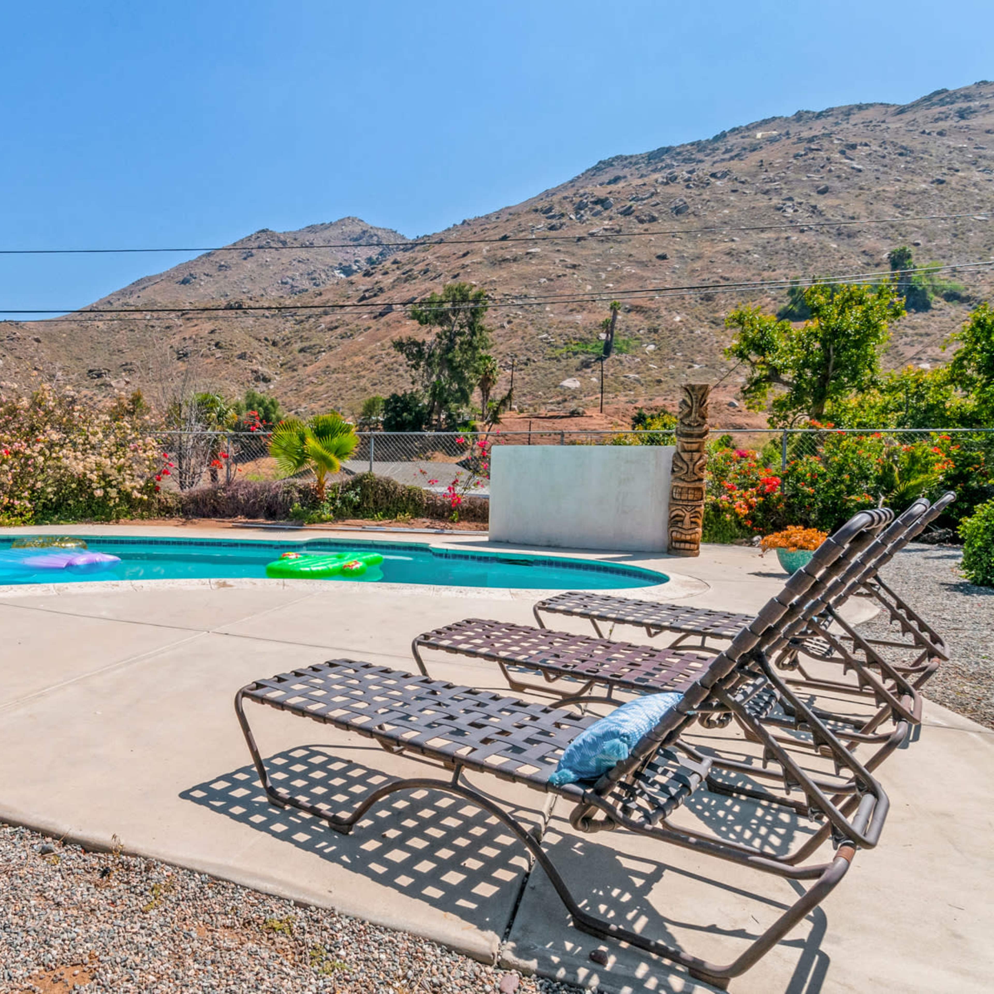 A swimming pool surrounded by lounge chairs, with mountains and desert vegetation in the background.