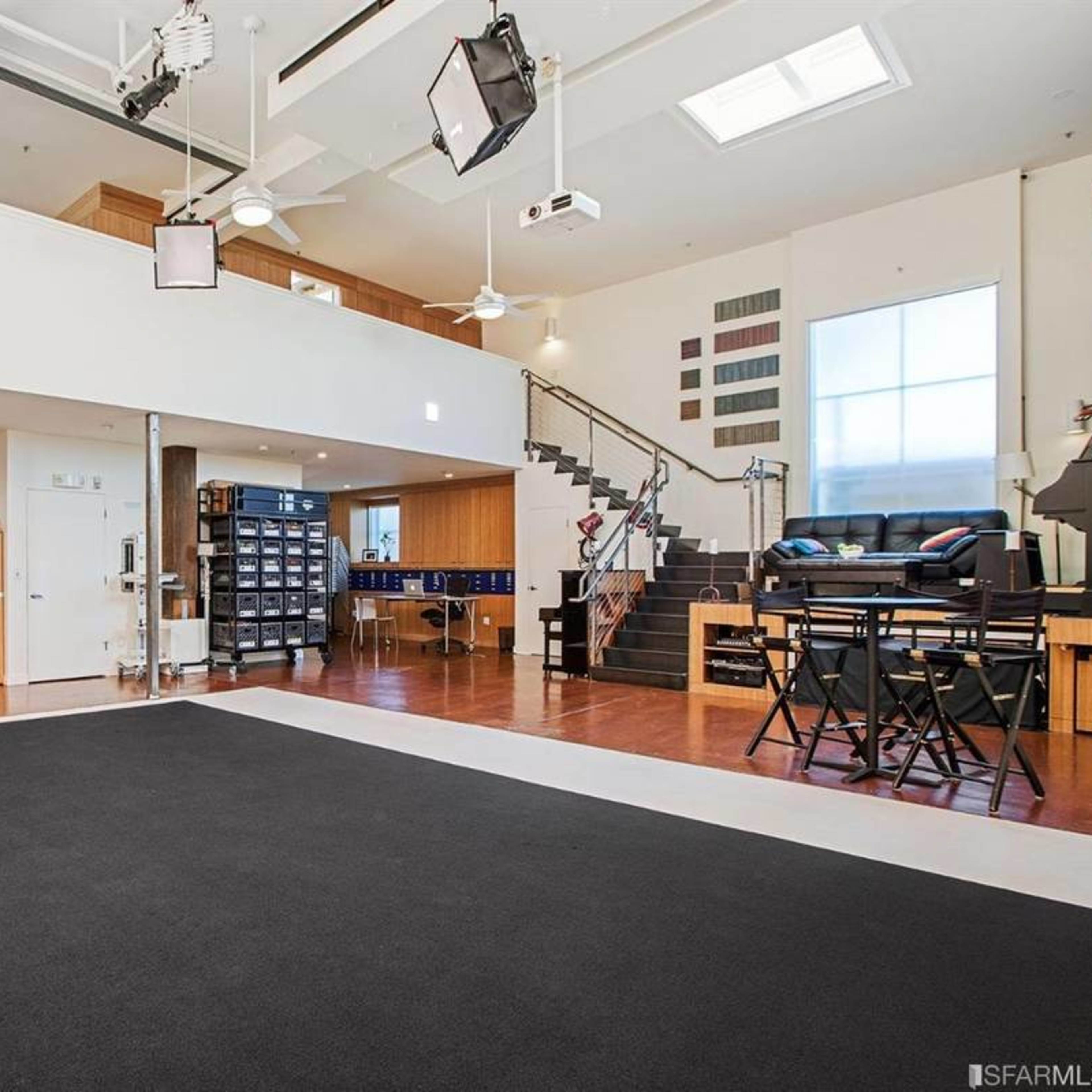 A spacious, modern room with a black area rug, a kitchen bar area, and a staircase leading to an upper level.
