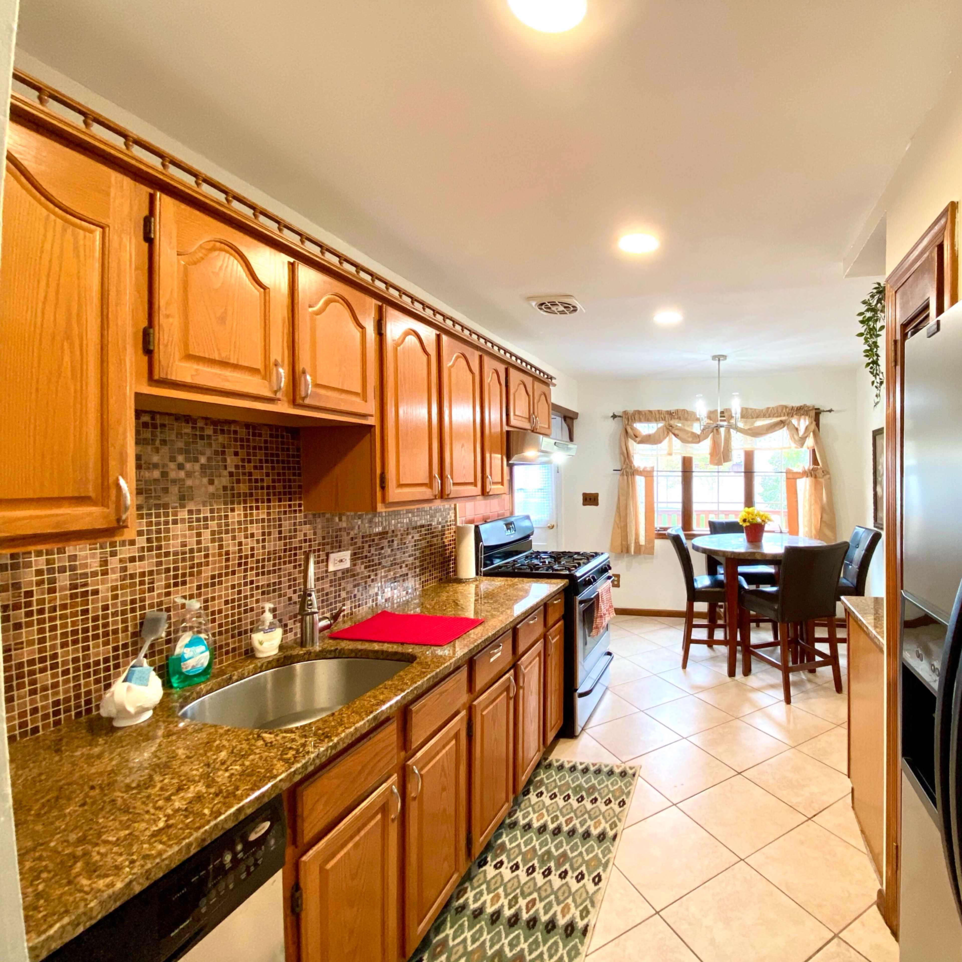 A kitchen features wooden cabinets, a granite countertop, a gas stove, a sink, and a dining table with chairs.