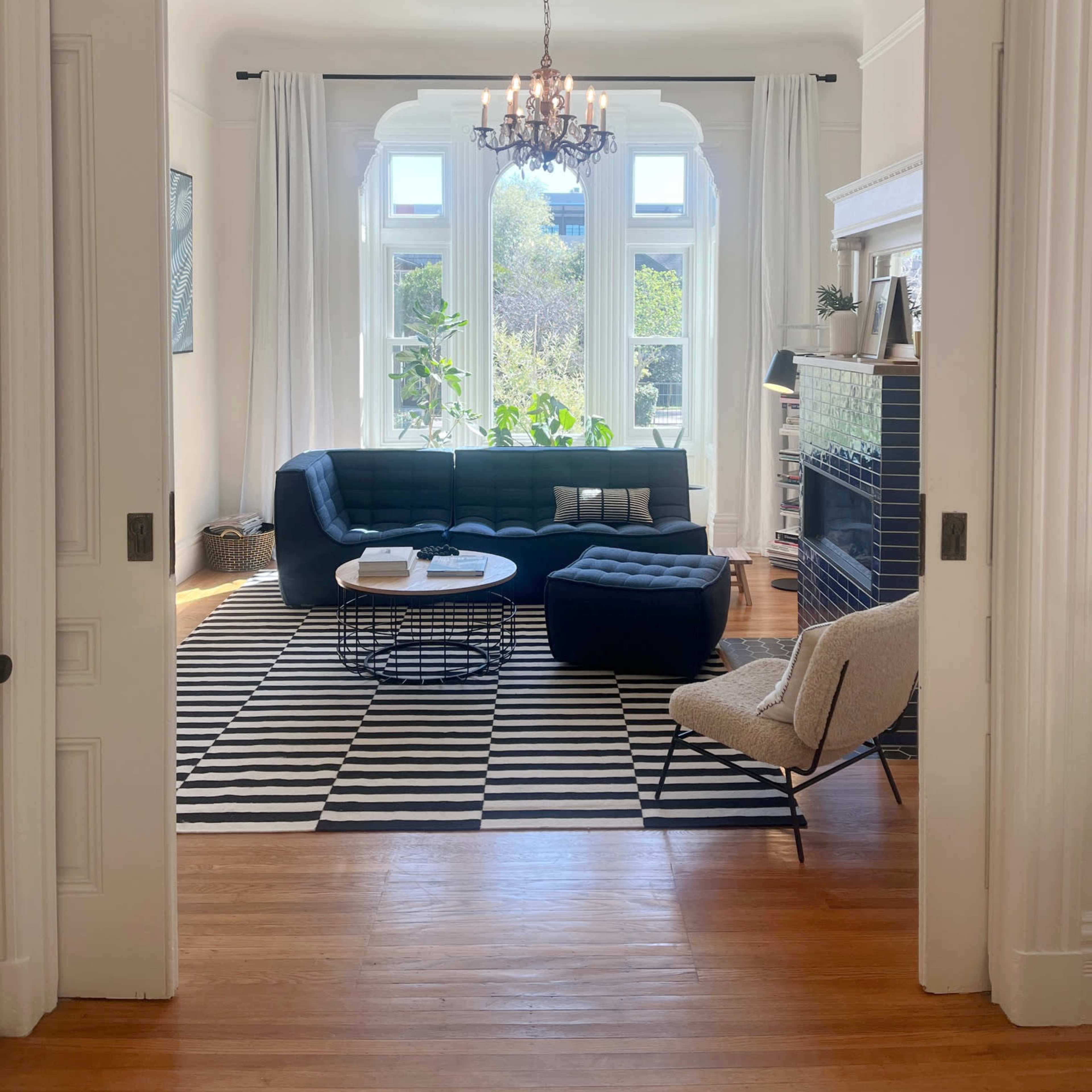 A well-lit living room with a navy blue sofa, a striped rug, and large windows around the seating area.