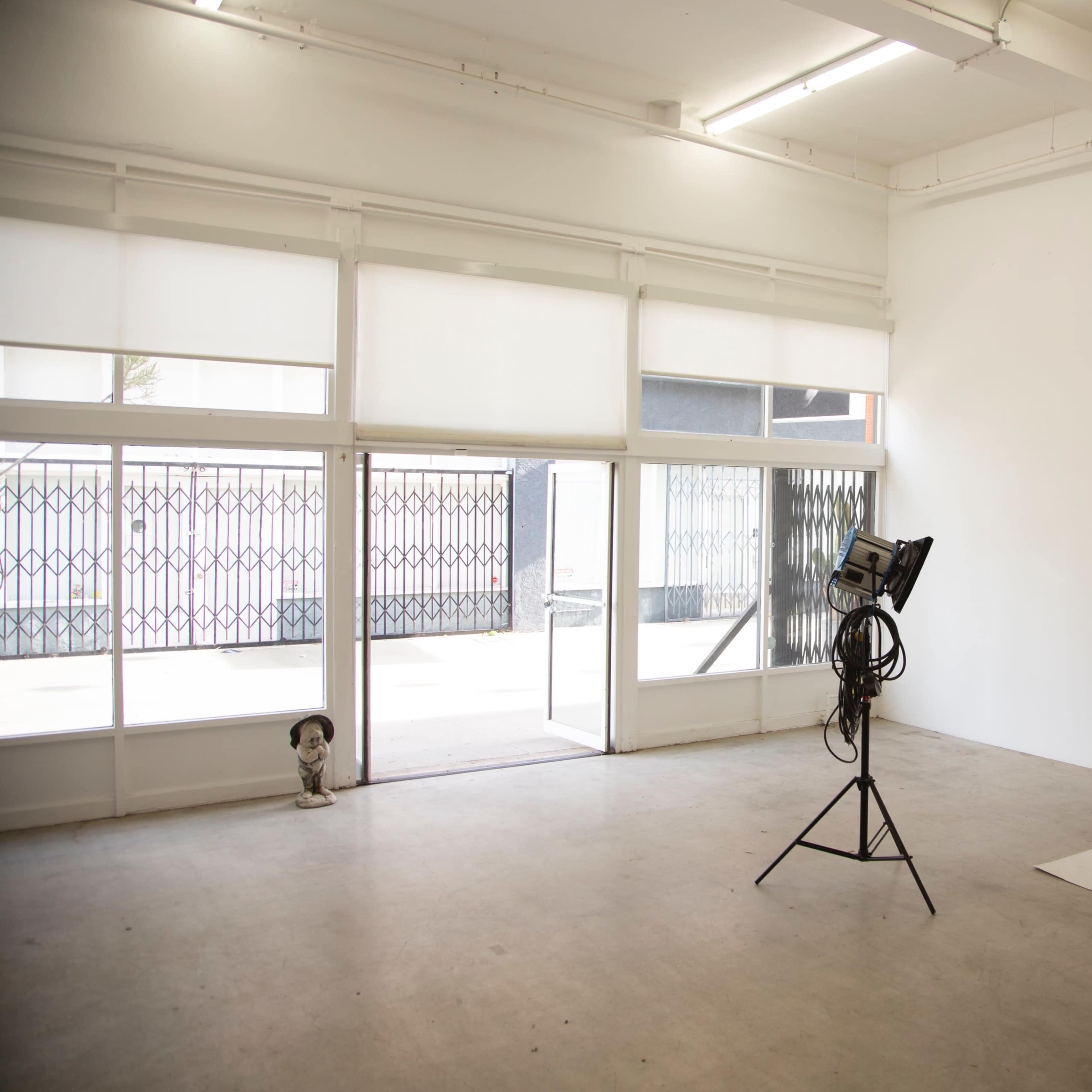 A spacious, empty studio with large windows, a light on a stand, and a white backdrop against the wall.