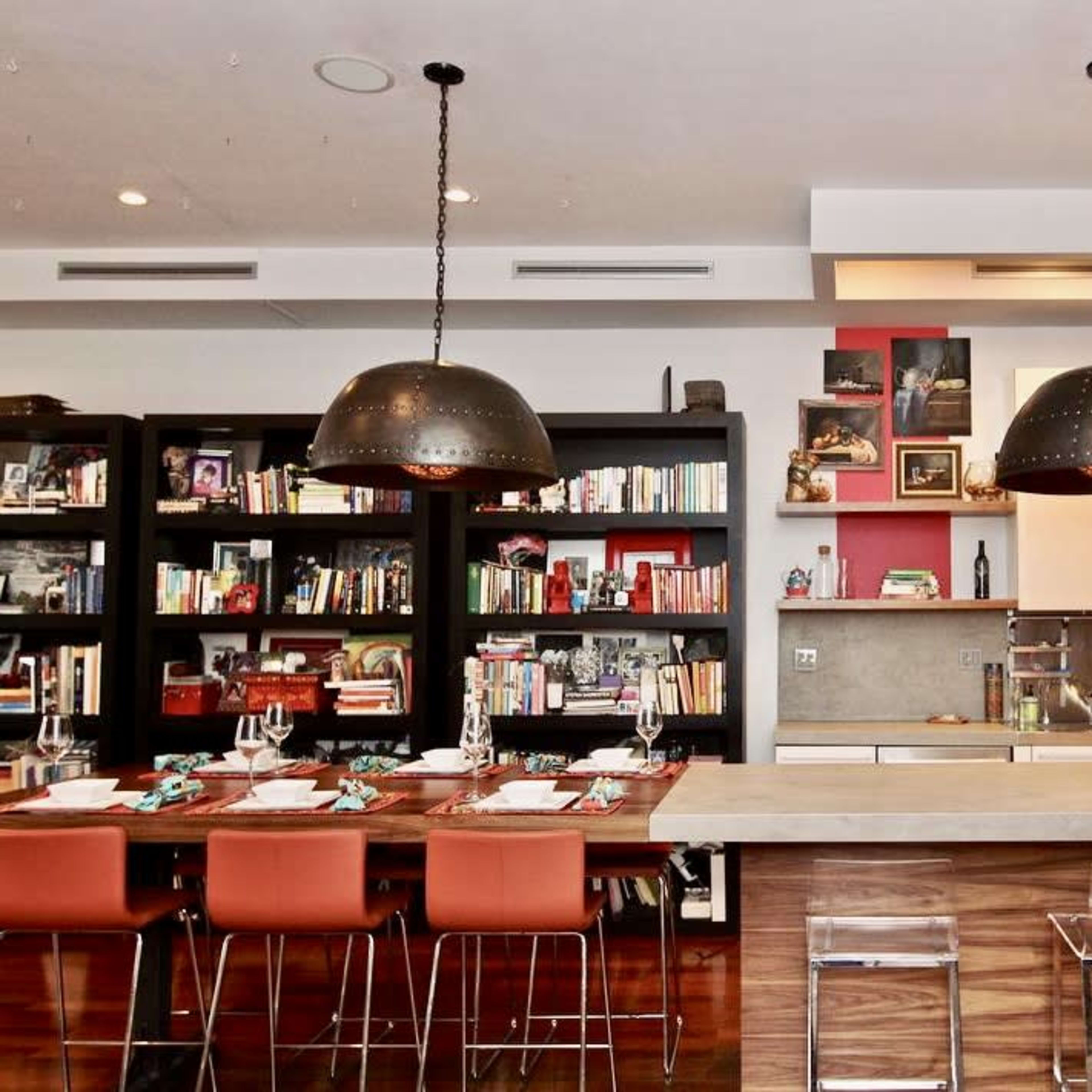 A modern kitchen with a large central island, two hanging pendant lights, and a dining area with a wooden table surrounded by orange chairs.