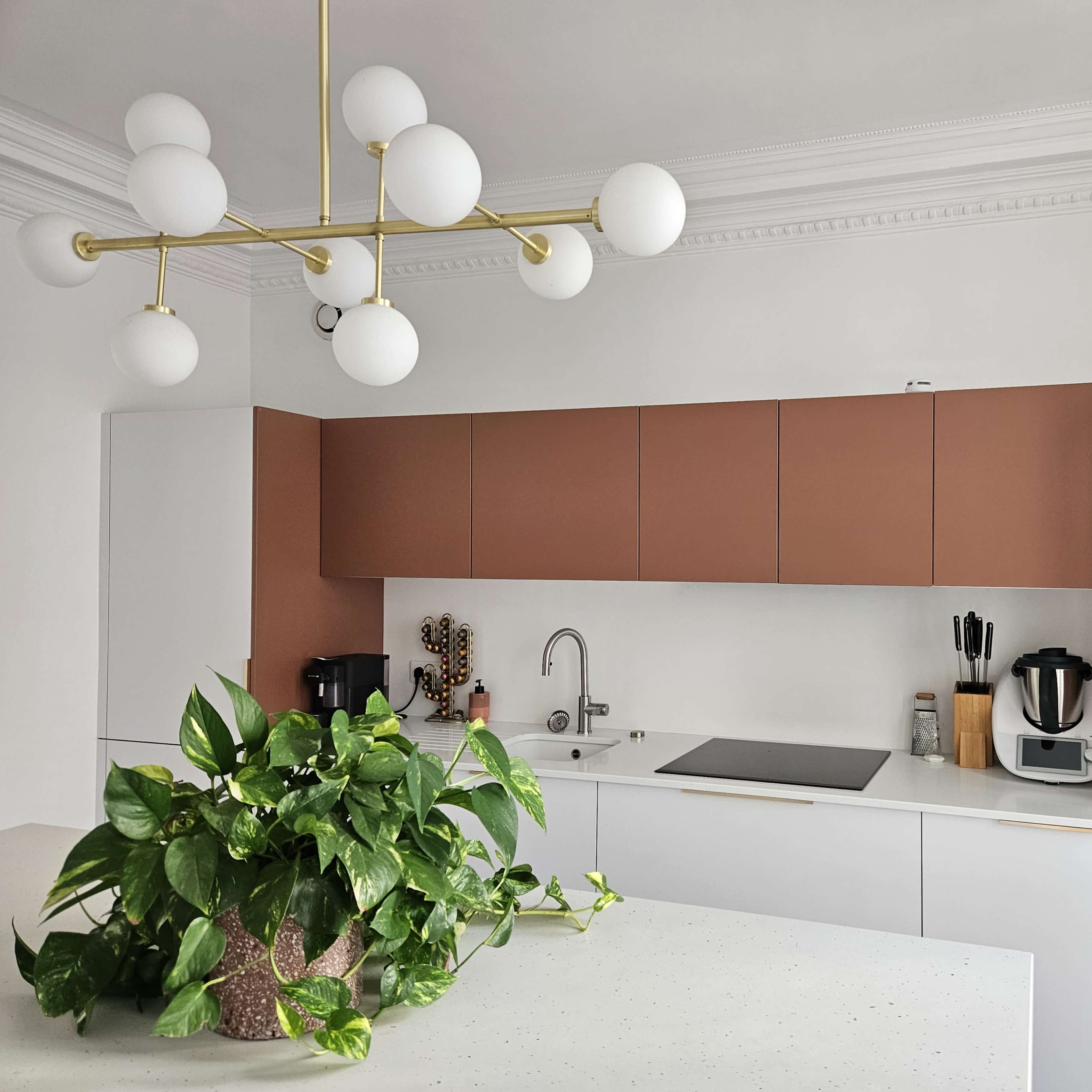 A modern kitchen features a mix of brown and white cabinetry, a central island with a plant centerpiece, and various appliances including a coffee maker and a blender.