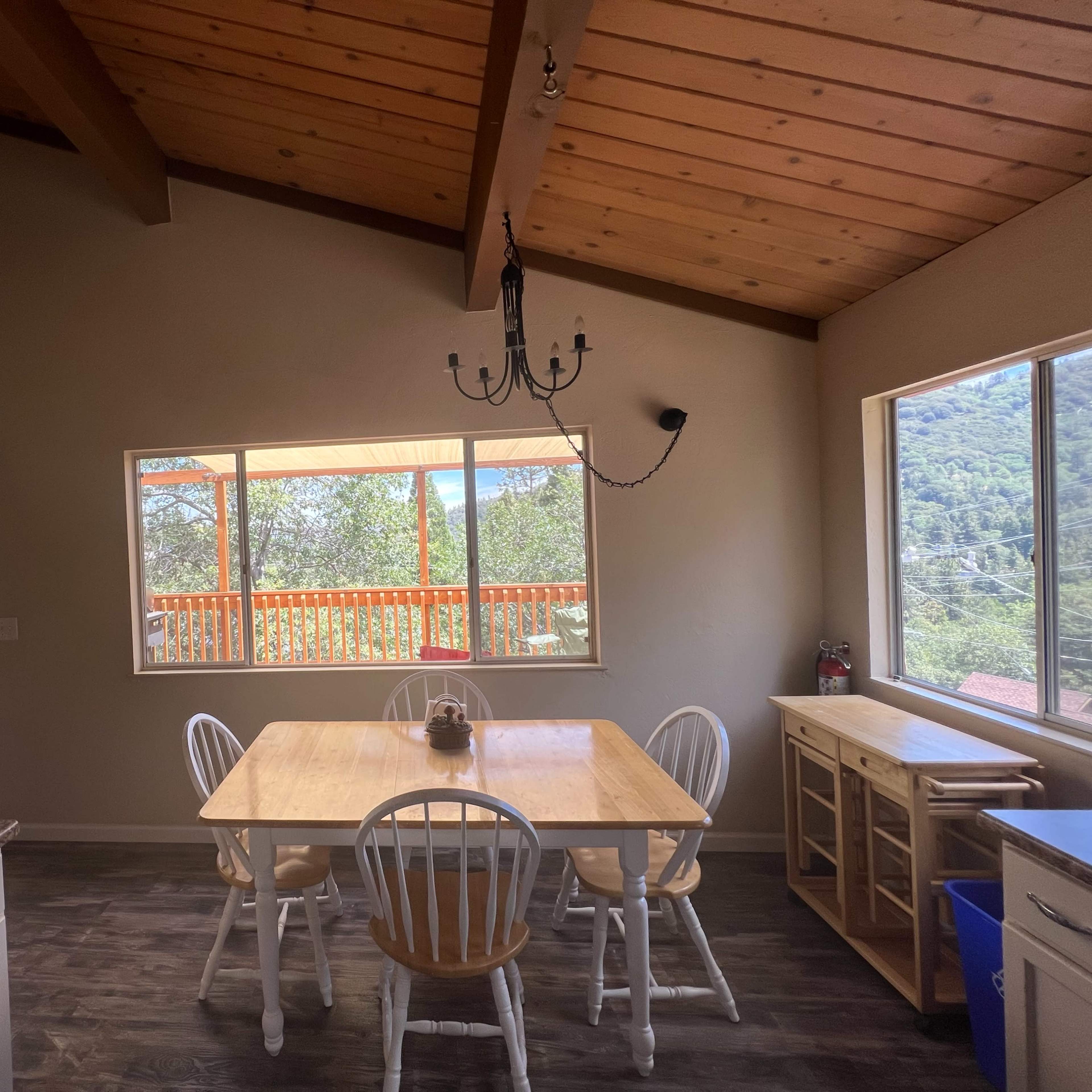 A bright, open dining area features a wooden table and chairs, with large windows overlooking a wooded landscape.