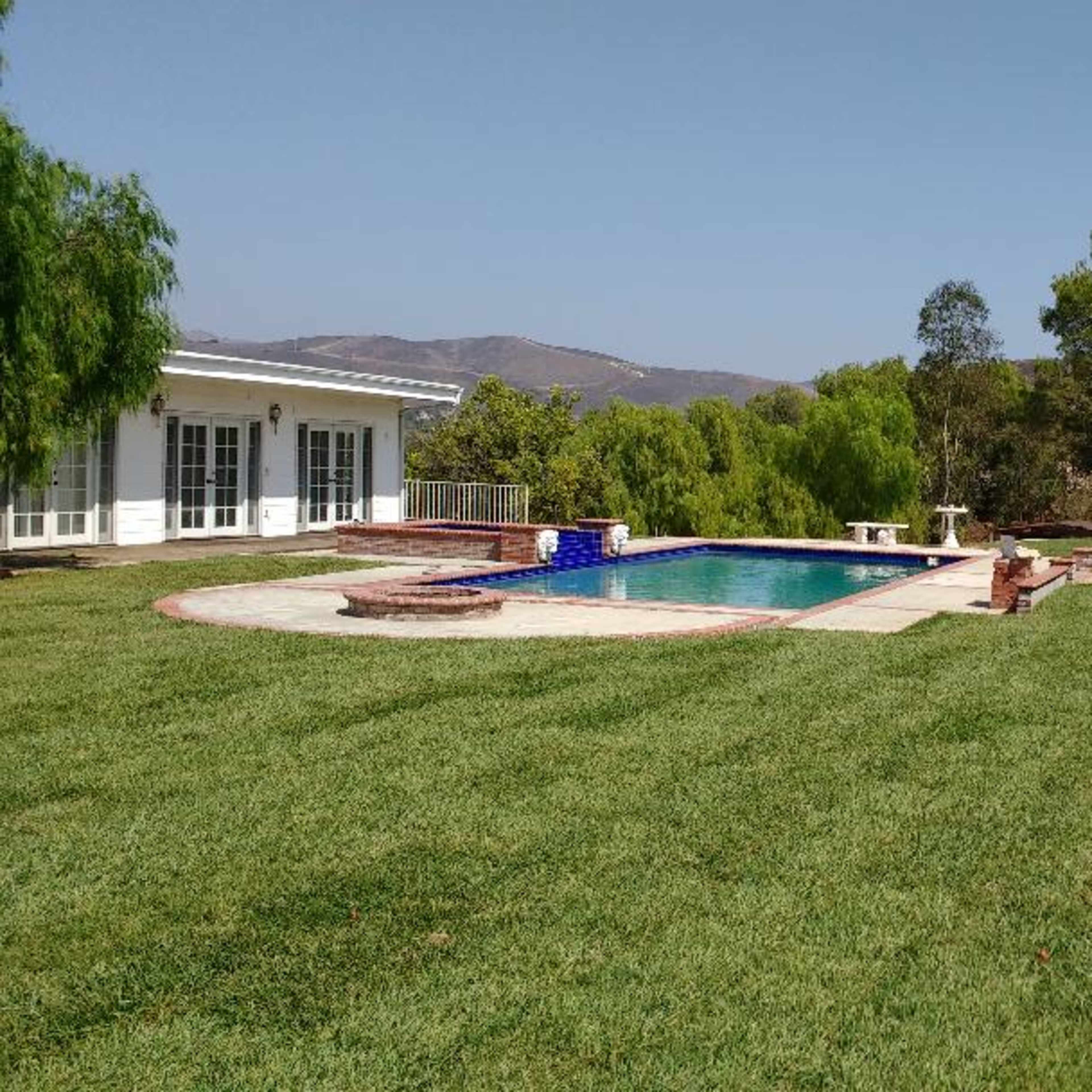 A spacious backyard with a swimming pool, grassy areas, and surrounding trees in a residential setting.