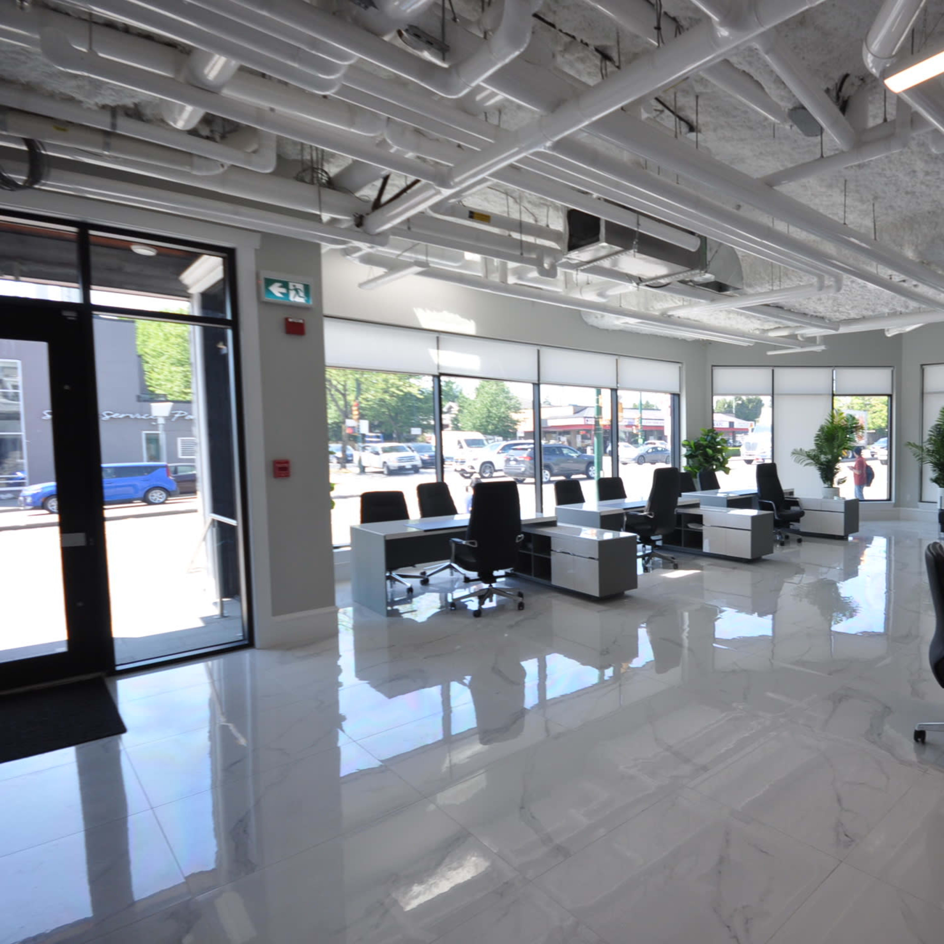 A modern office space with white walls, large windows, and multiple workstations arranged with black office chairs.