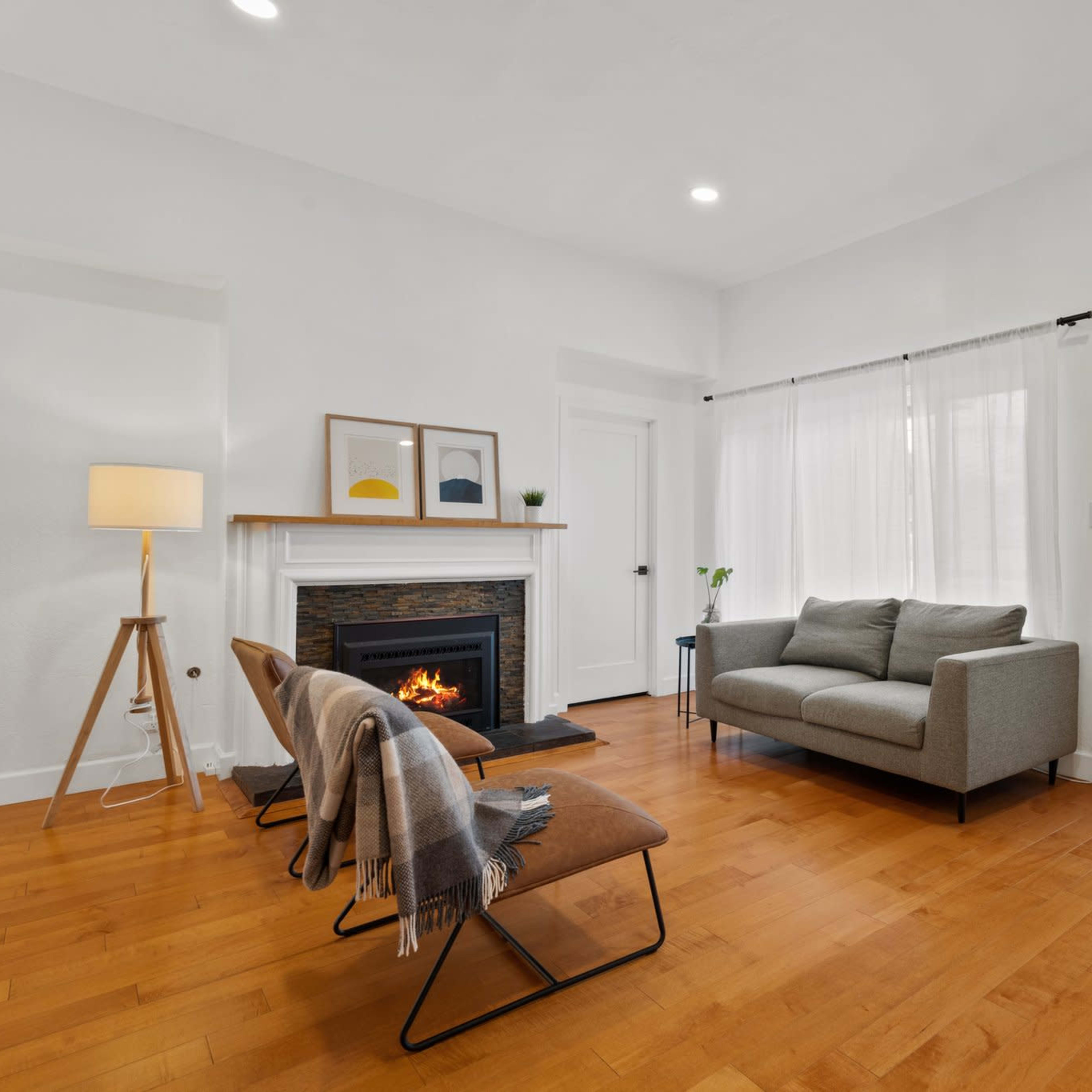 A modern living room with a gray sofa, two chairs with blankets, a fireplace, and a wooden door featuring horizontal glass panels.