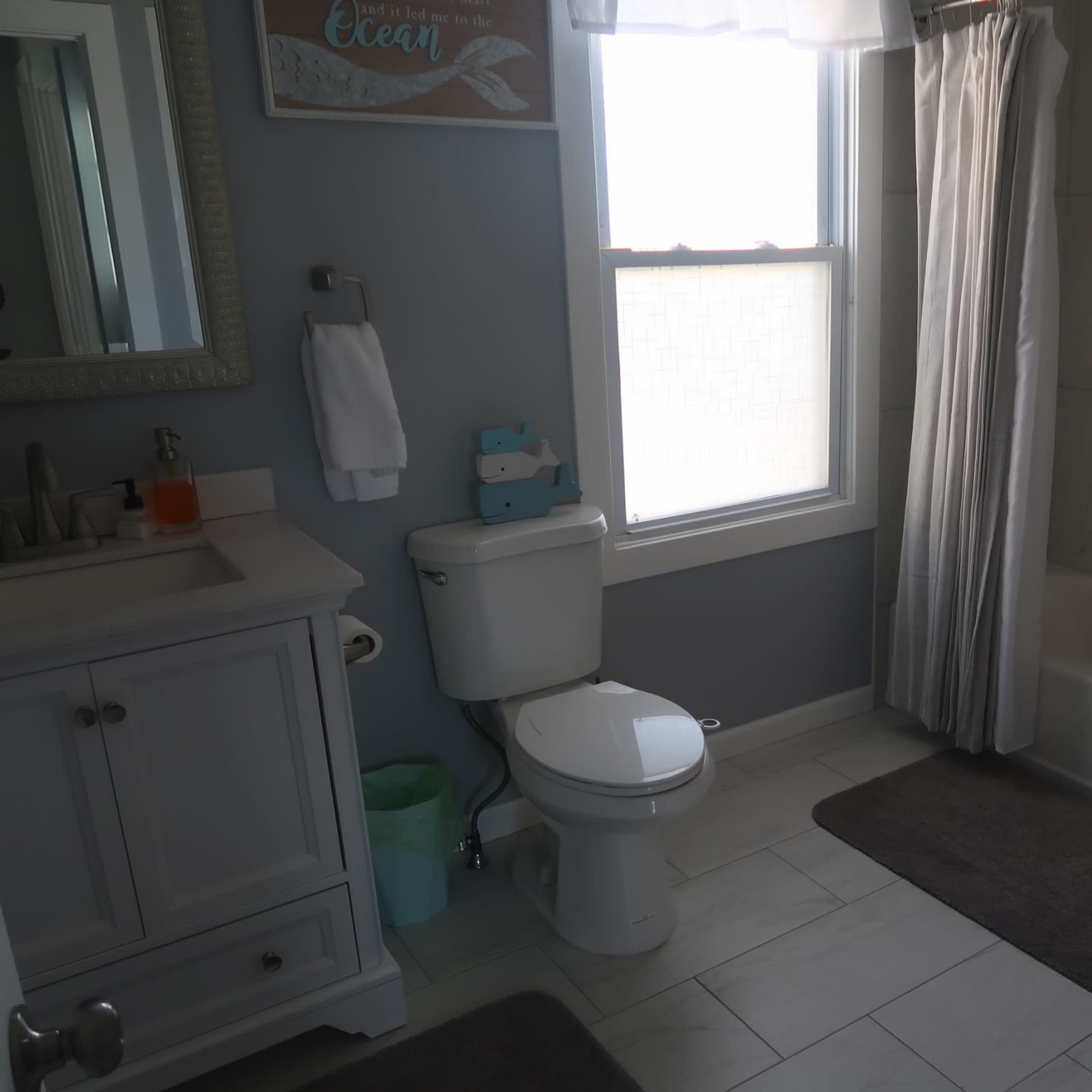 A bathroom featuring a toilet, bathtub with a shower curtain, sink with a mirrored cabinet, and light-colored tiled flooring.