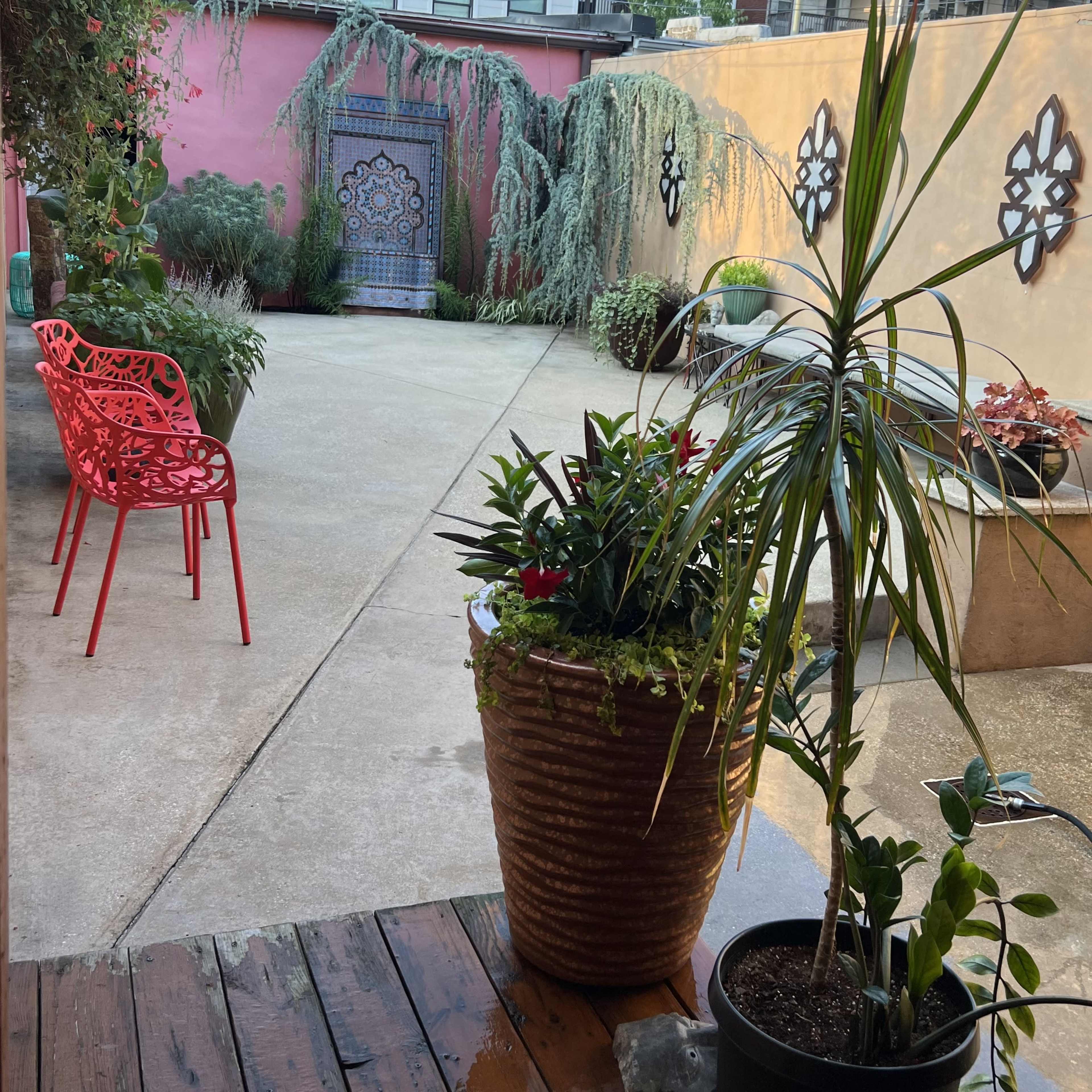A courtyard with potted plants, a red chair, and a colorful decorative door in the background.