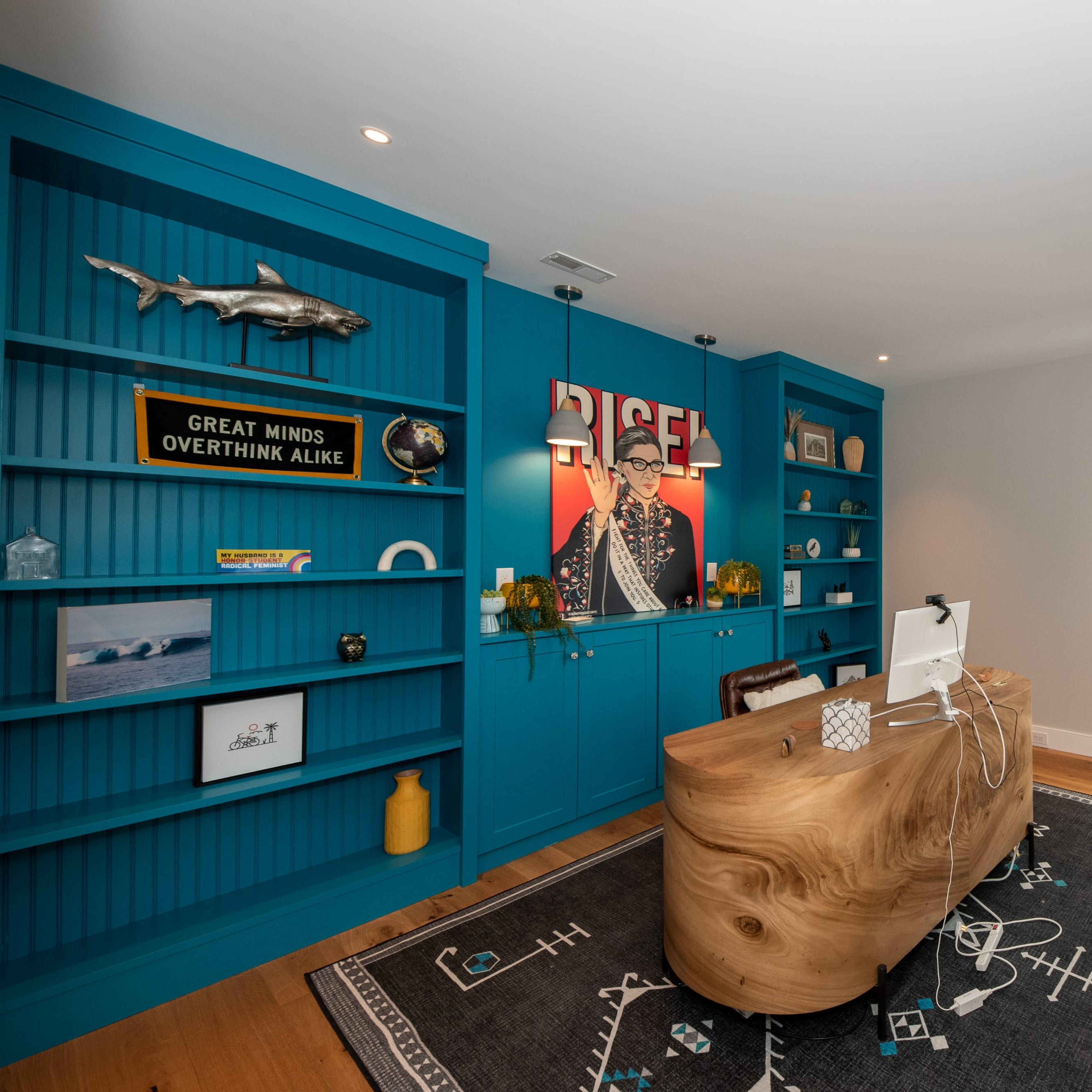 A modern office with bright blue built-in shelves, a large wooden desk, and a stylish area rug.