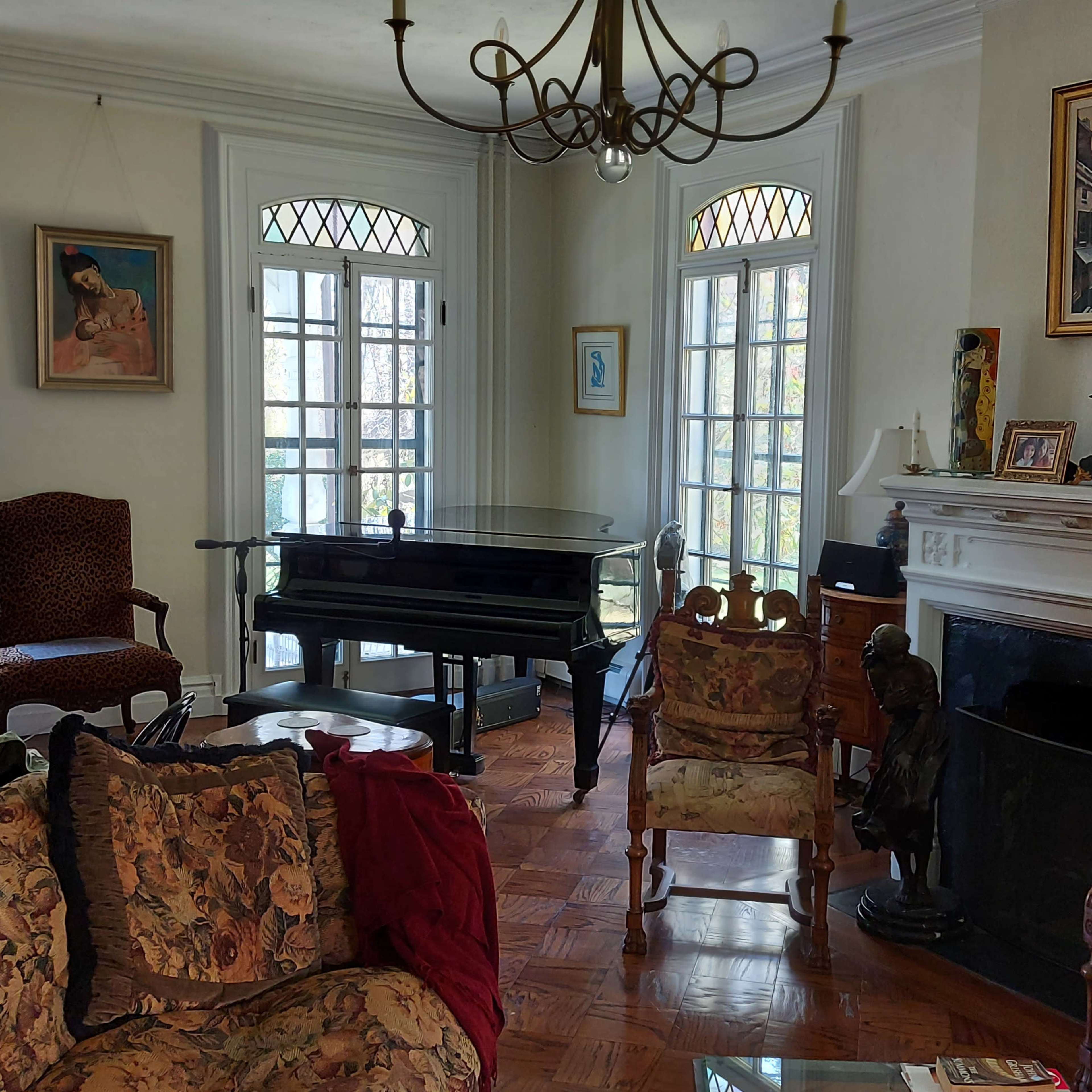 A spacious living room with a grand piano, several ornate chairs, and large windows allowing natural light to illuminate the space.