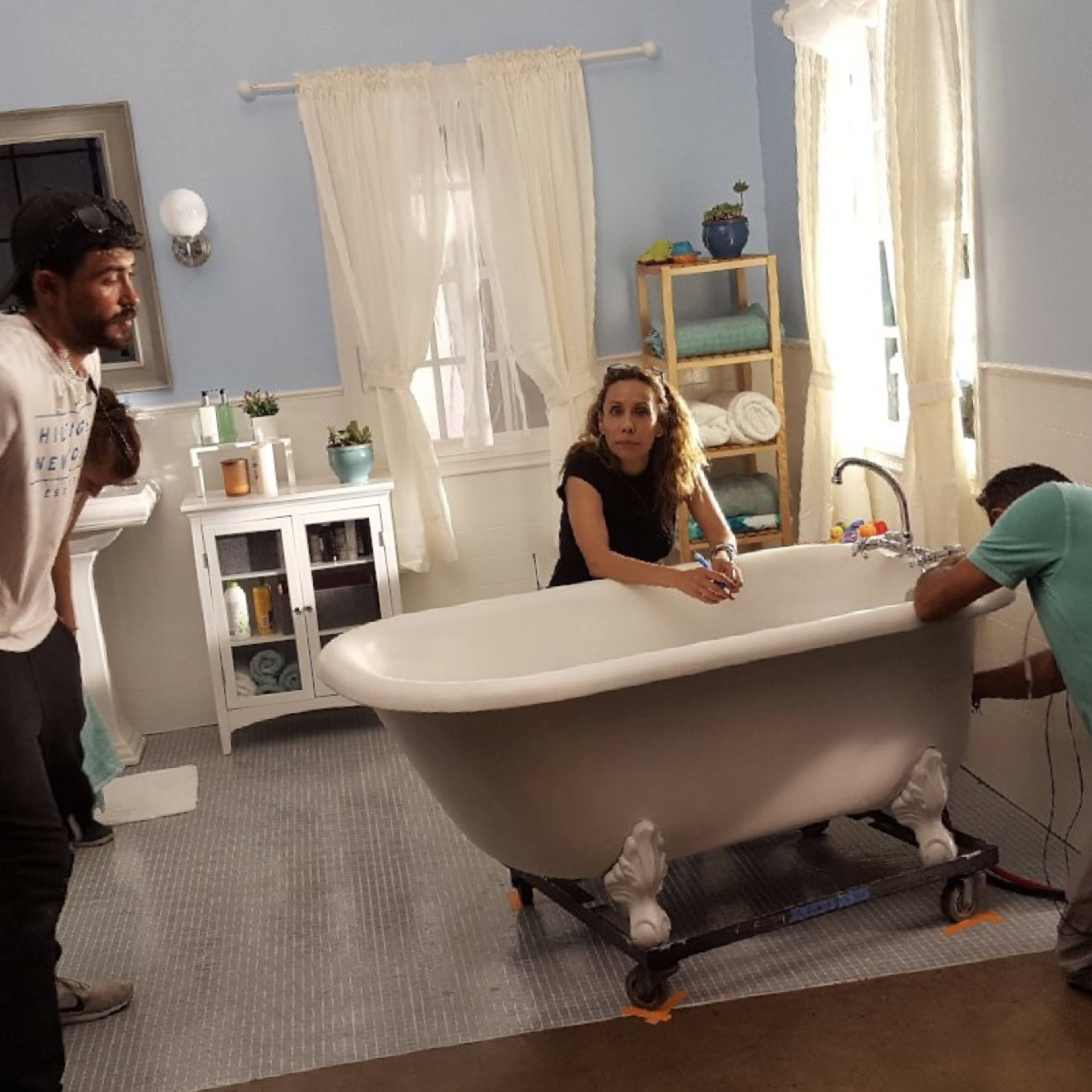 Three people are working in a well-lit bathroom with a freestanding bathtub, one person is adjusting the faucet while another is crouched down near the plumbing.