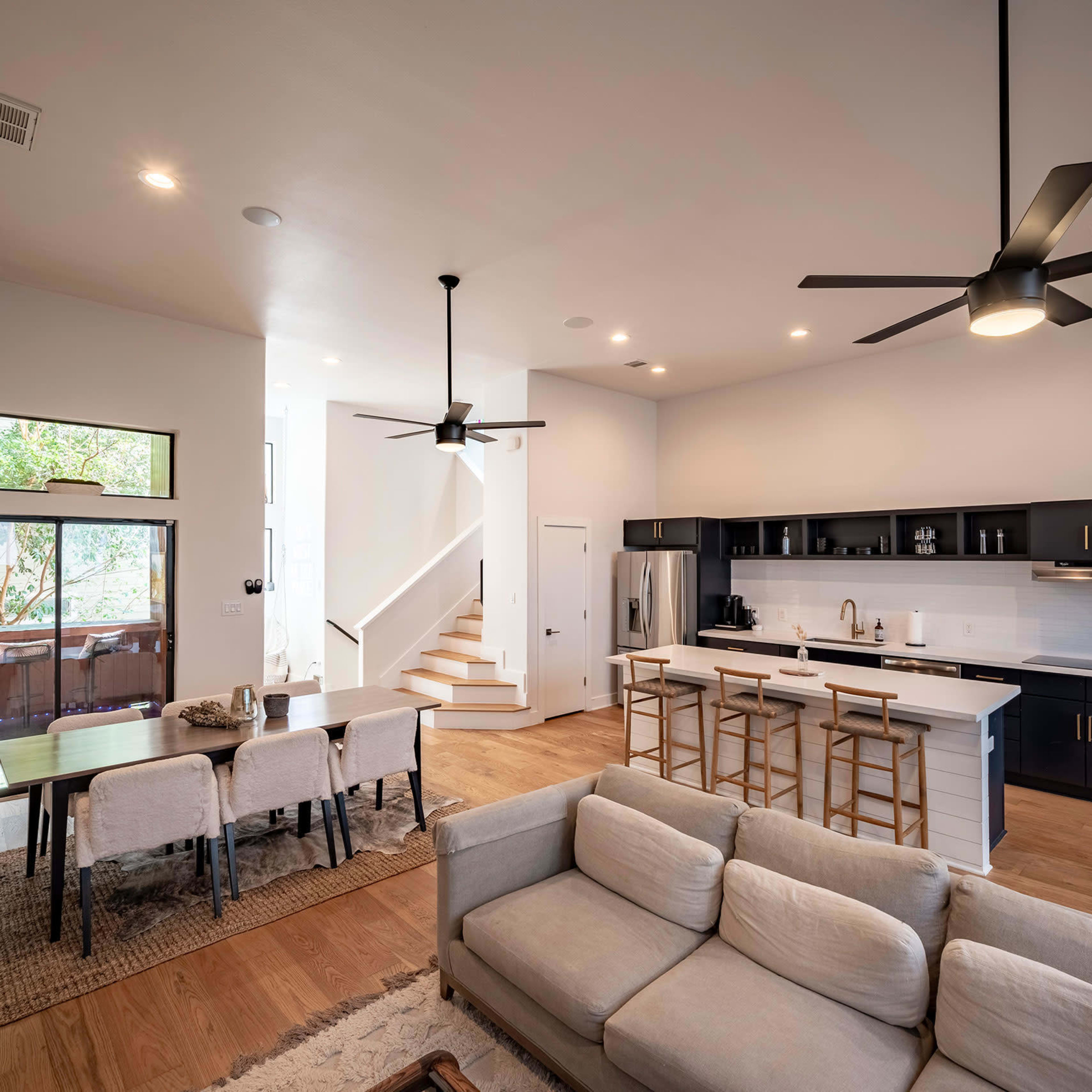 A modern open-concept living space featuring a kitchen, dining area, and seating area with a staircase in the background.
