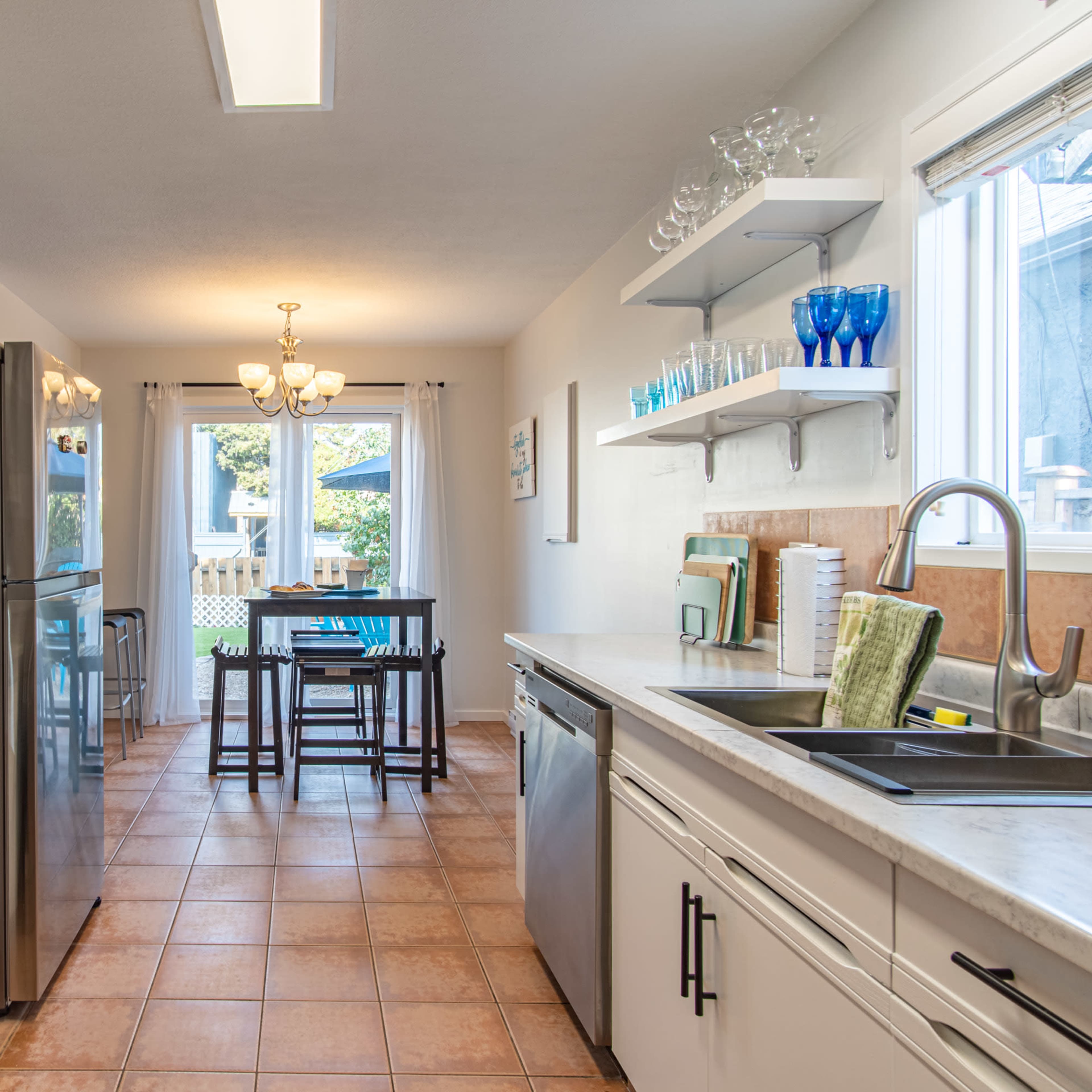 A modern kitchen features stainless steel appliances, light cabinetry, and a dining area with a table and chairs.
