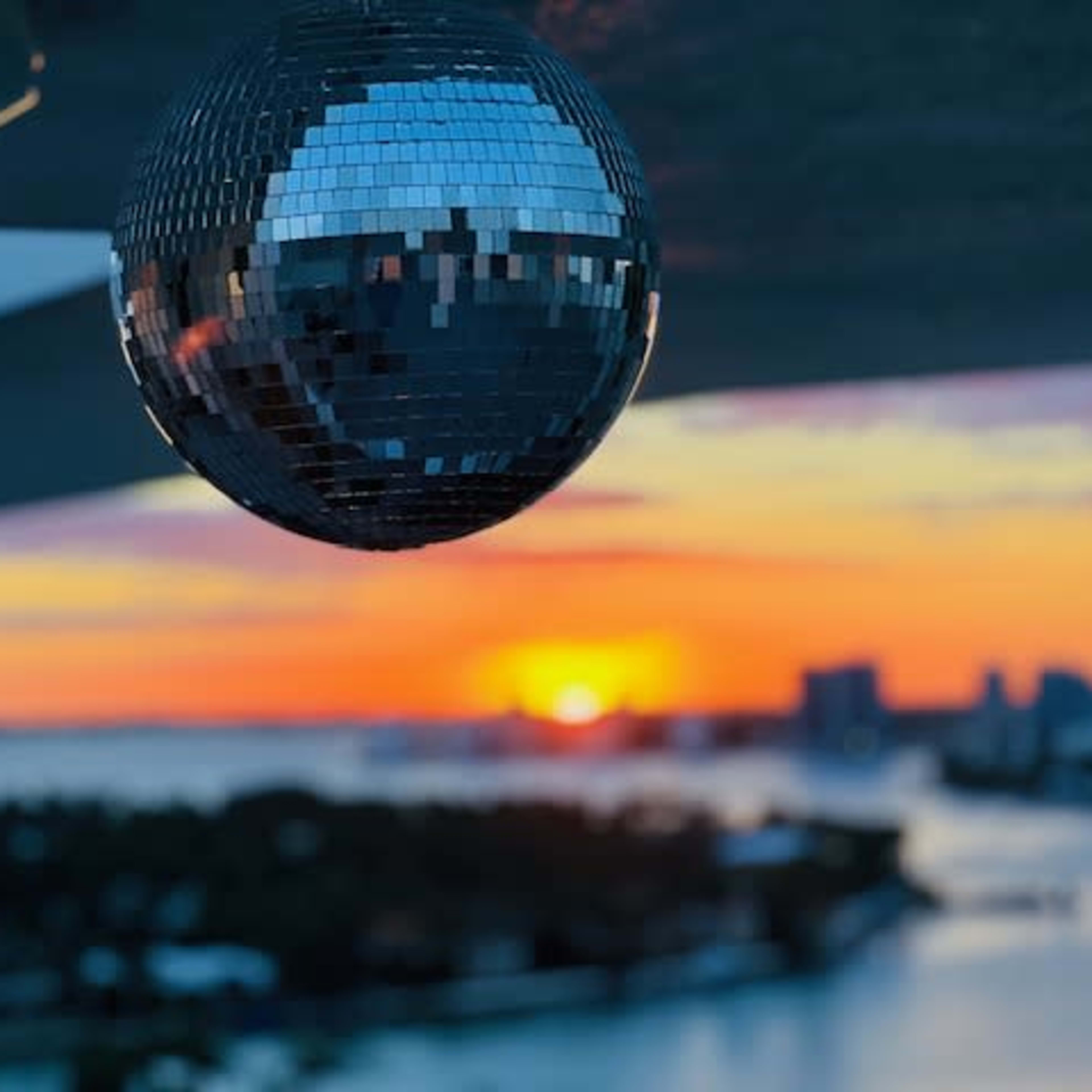 A disco ball hangs in the foreground as the sun sets over a waterfront city.