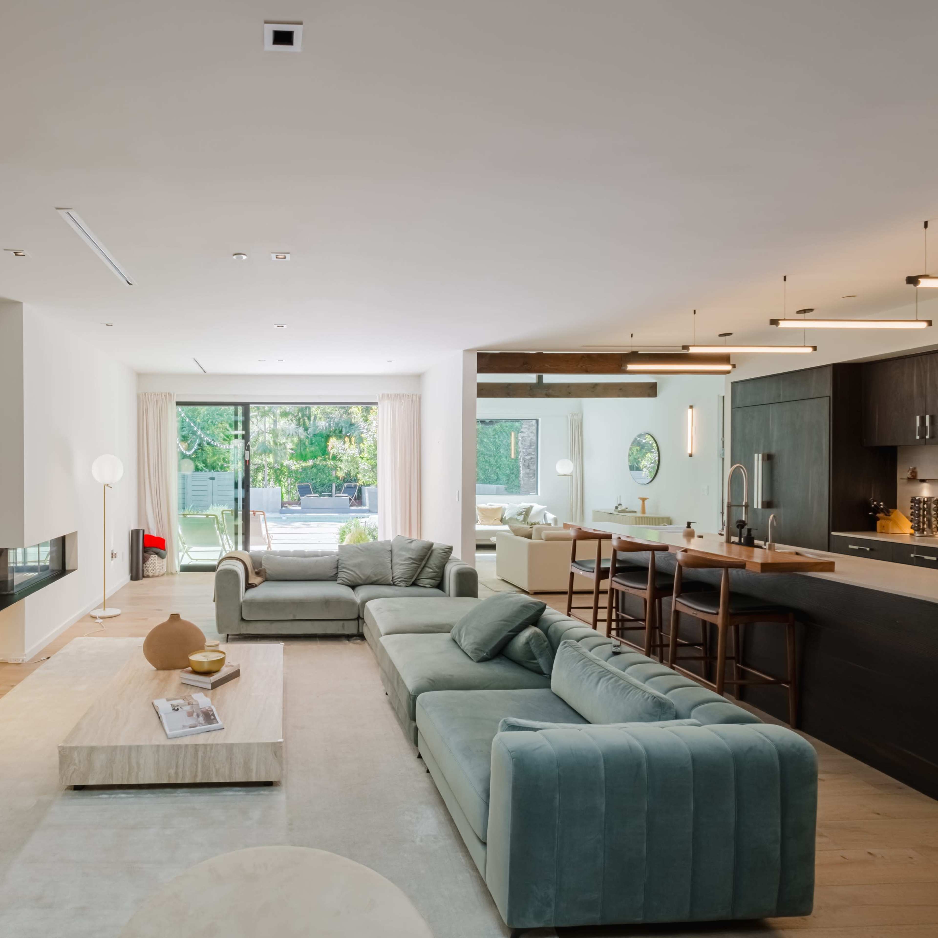 A modern living room with a sectional sofa, a coffee table, and a view of an open kitchen through large sliding glass doors.