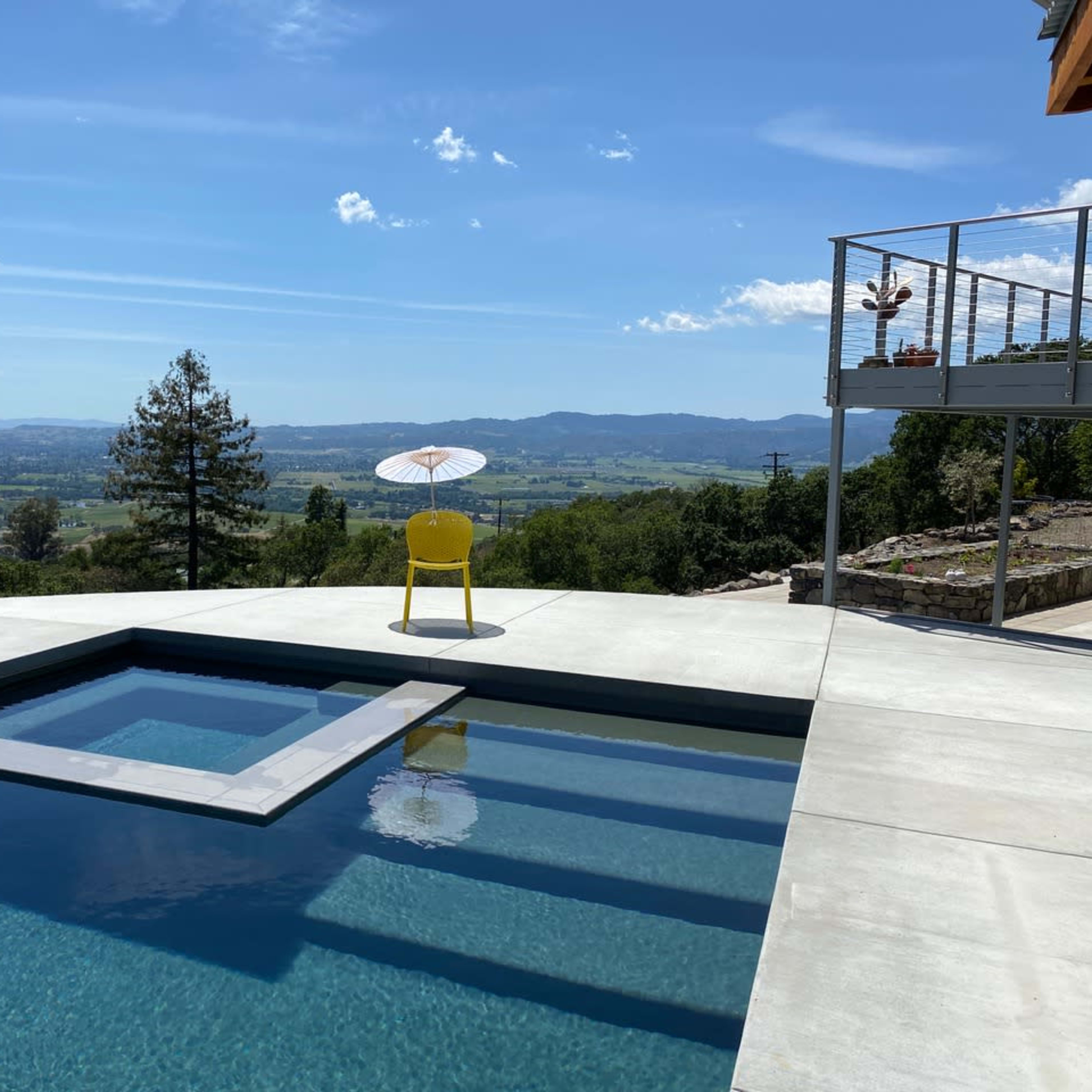 A yellow chair with a parasol sits next to a rectangular swimming pool overlooking a scenic valley.