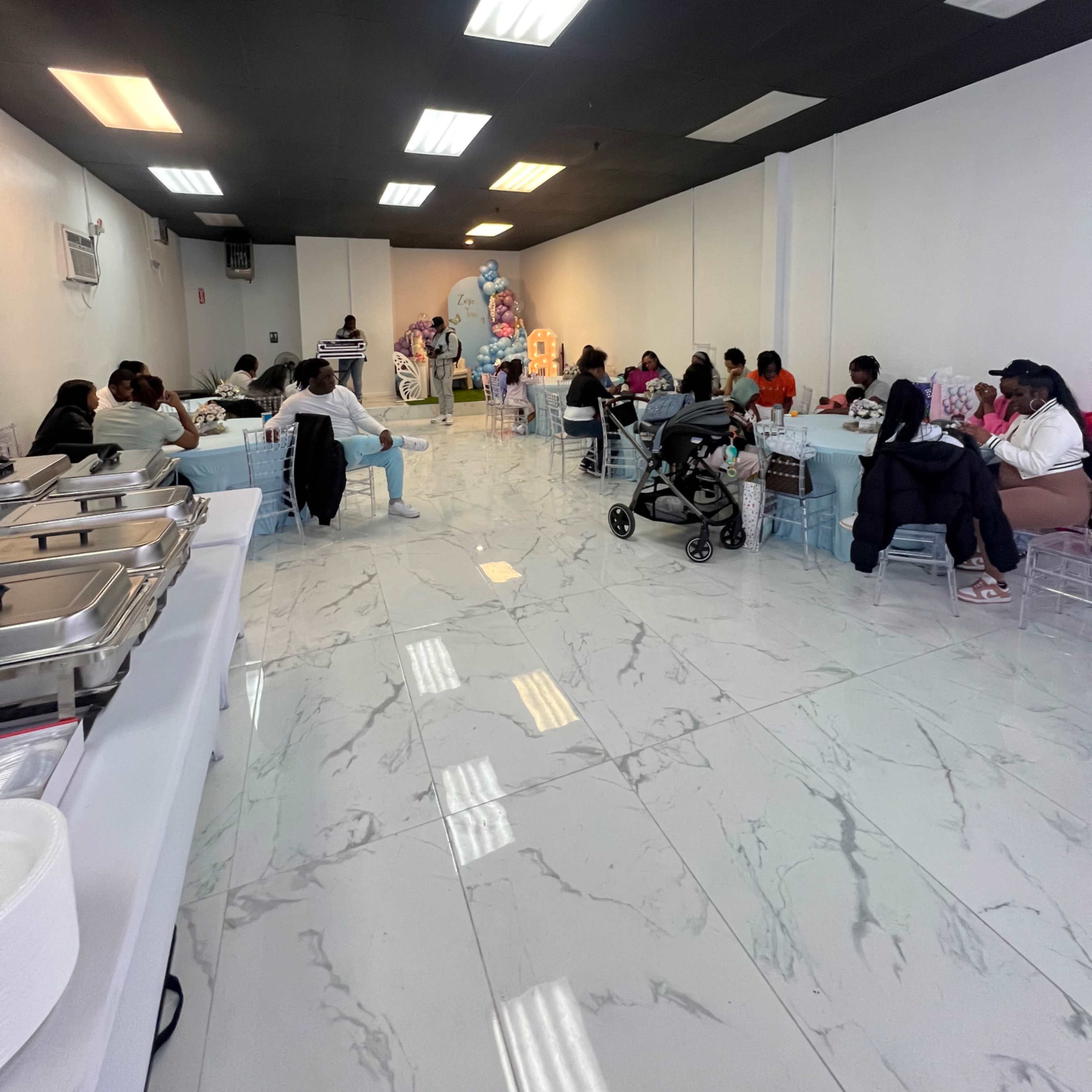 A spacious dining area with people seated at various tables while a buffet setup is visible on the left side.