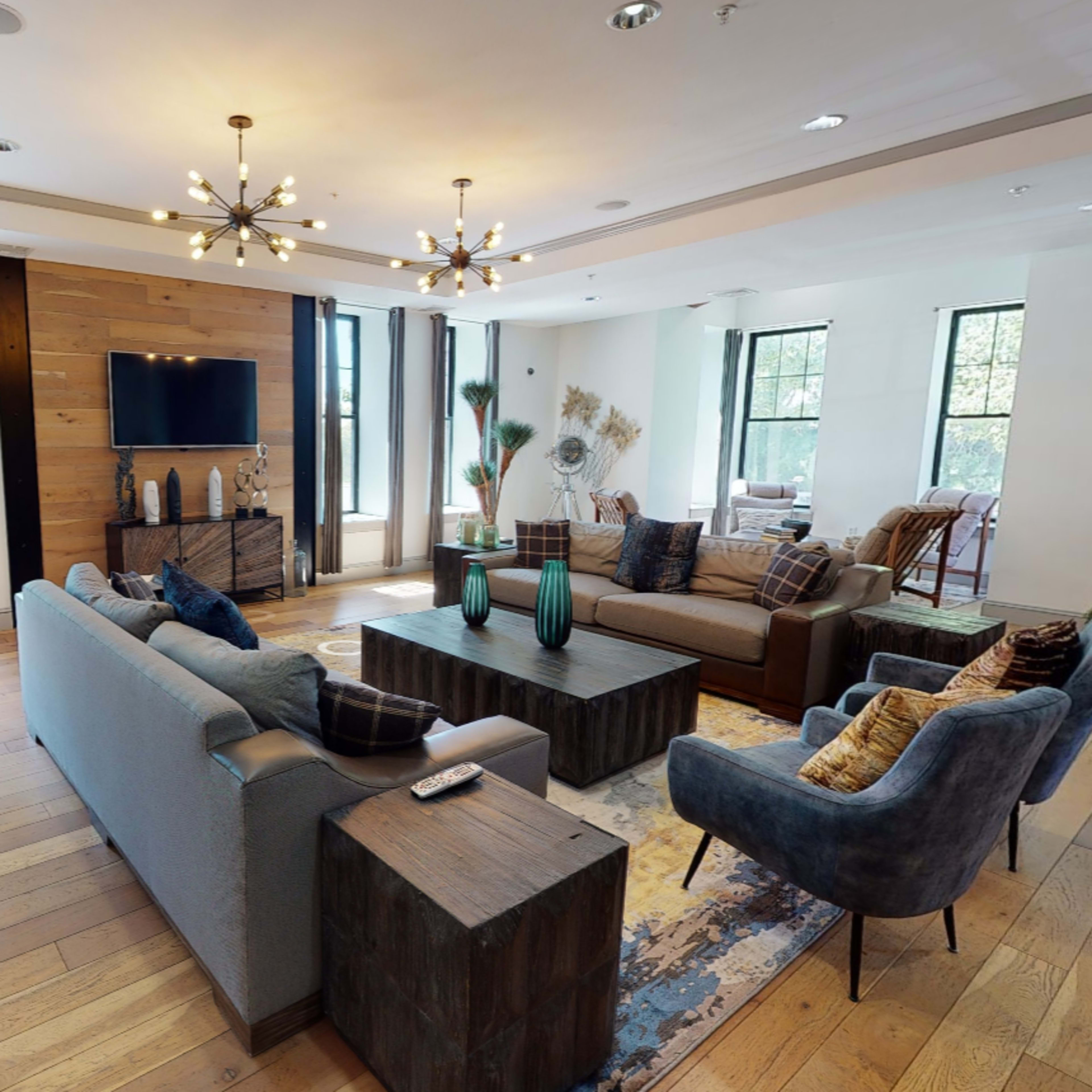 A modern living room features a large coffee table, comfortable seating areas, and windows with natural light.