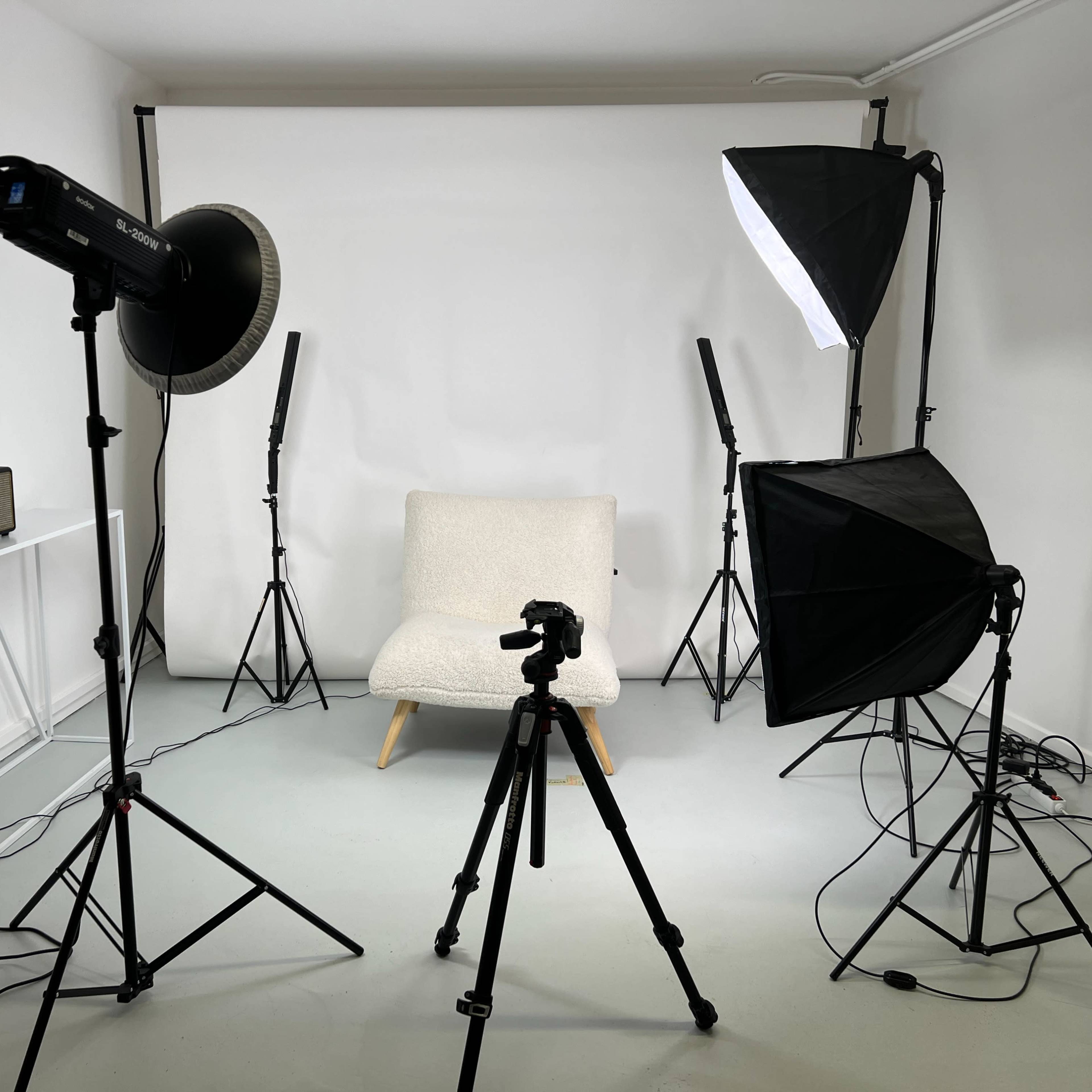 A photography studio setup features a light gray background, a chair in the center, and multiple lighting equipment arranged around it.