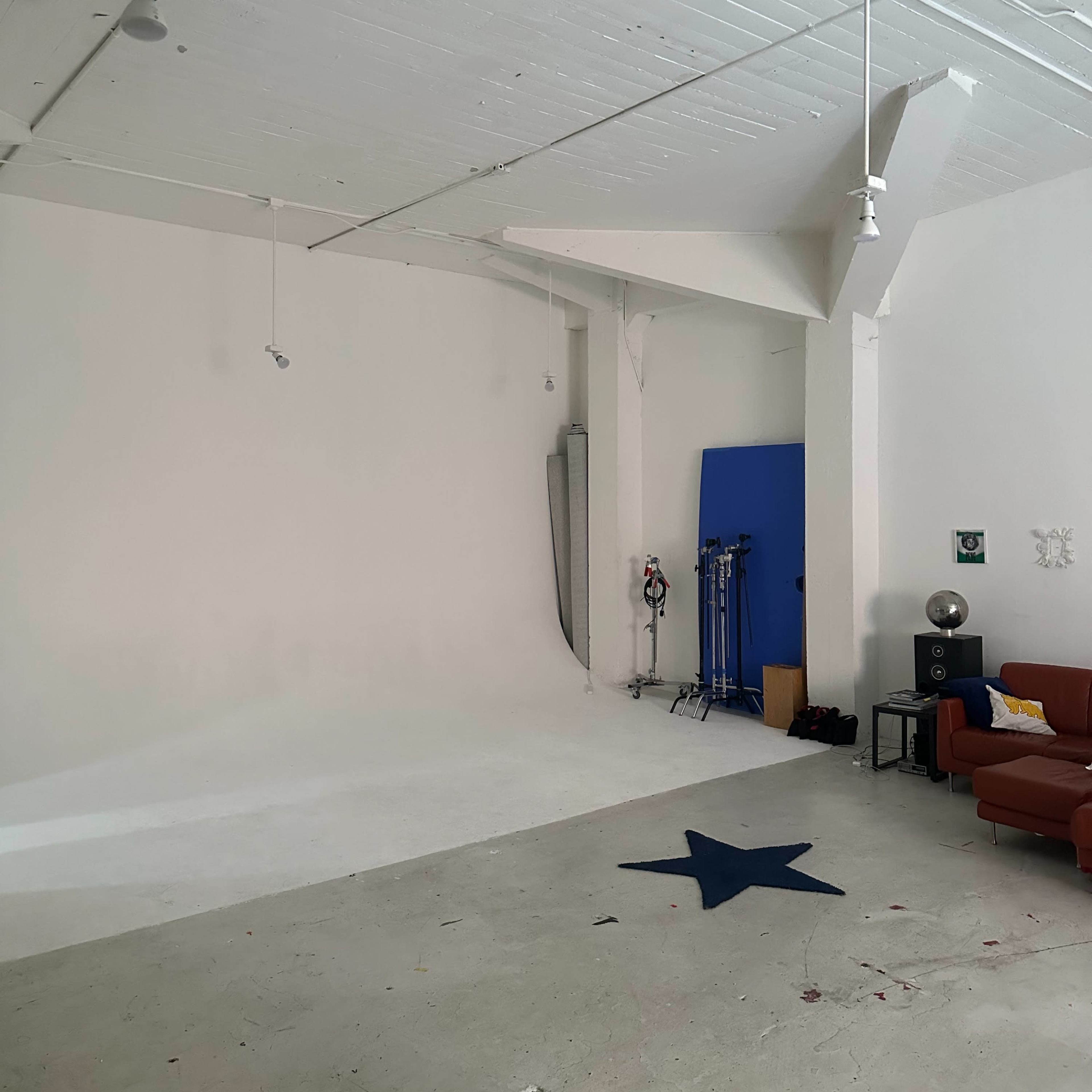 A spacious, empty studio with white walls, a light gray floor, and a blue backdrop leaning against the wall.