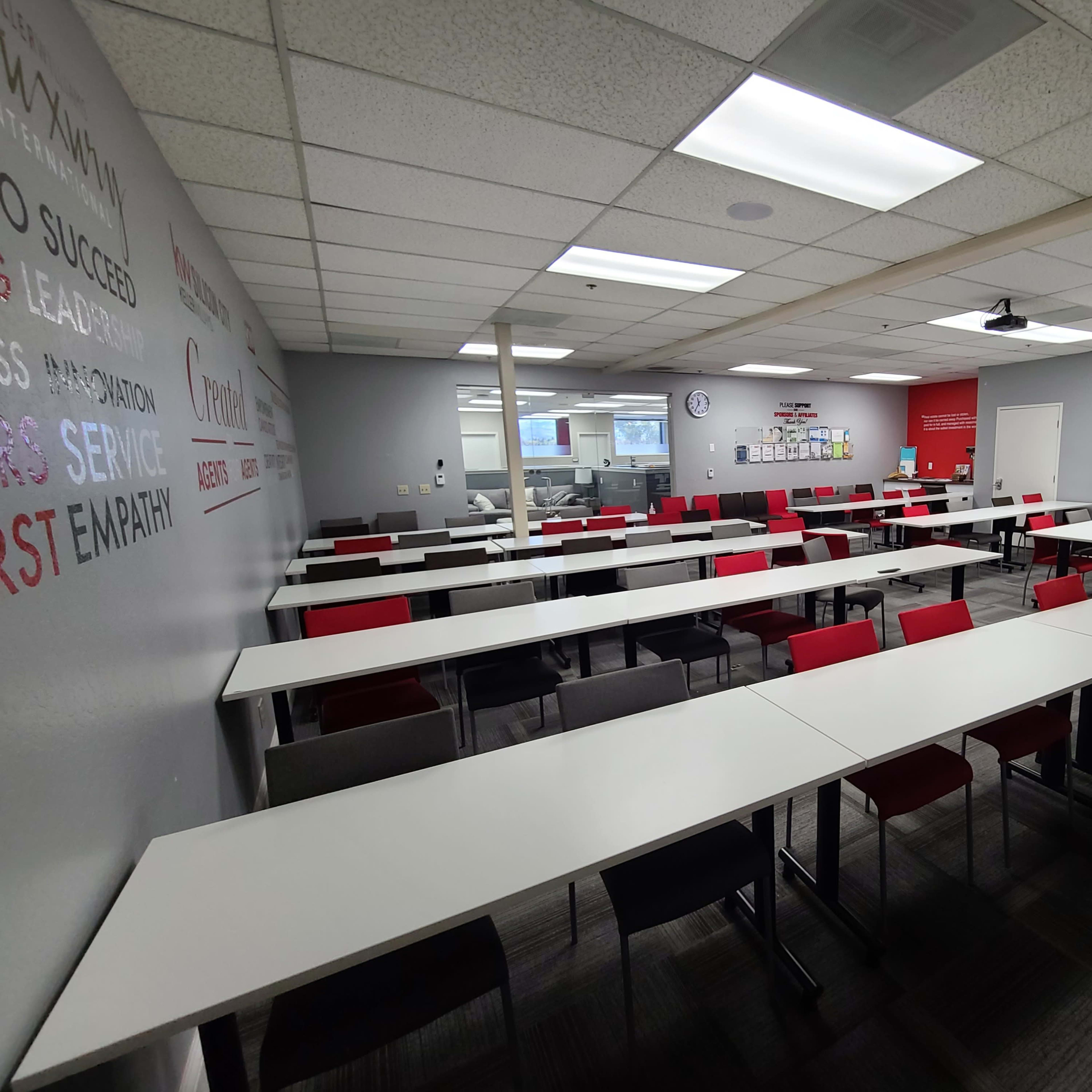 A classroom with multiple tables arranged in rows, equipped with chairs, a whiteboard, and a clock on the wall.