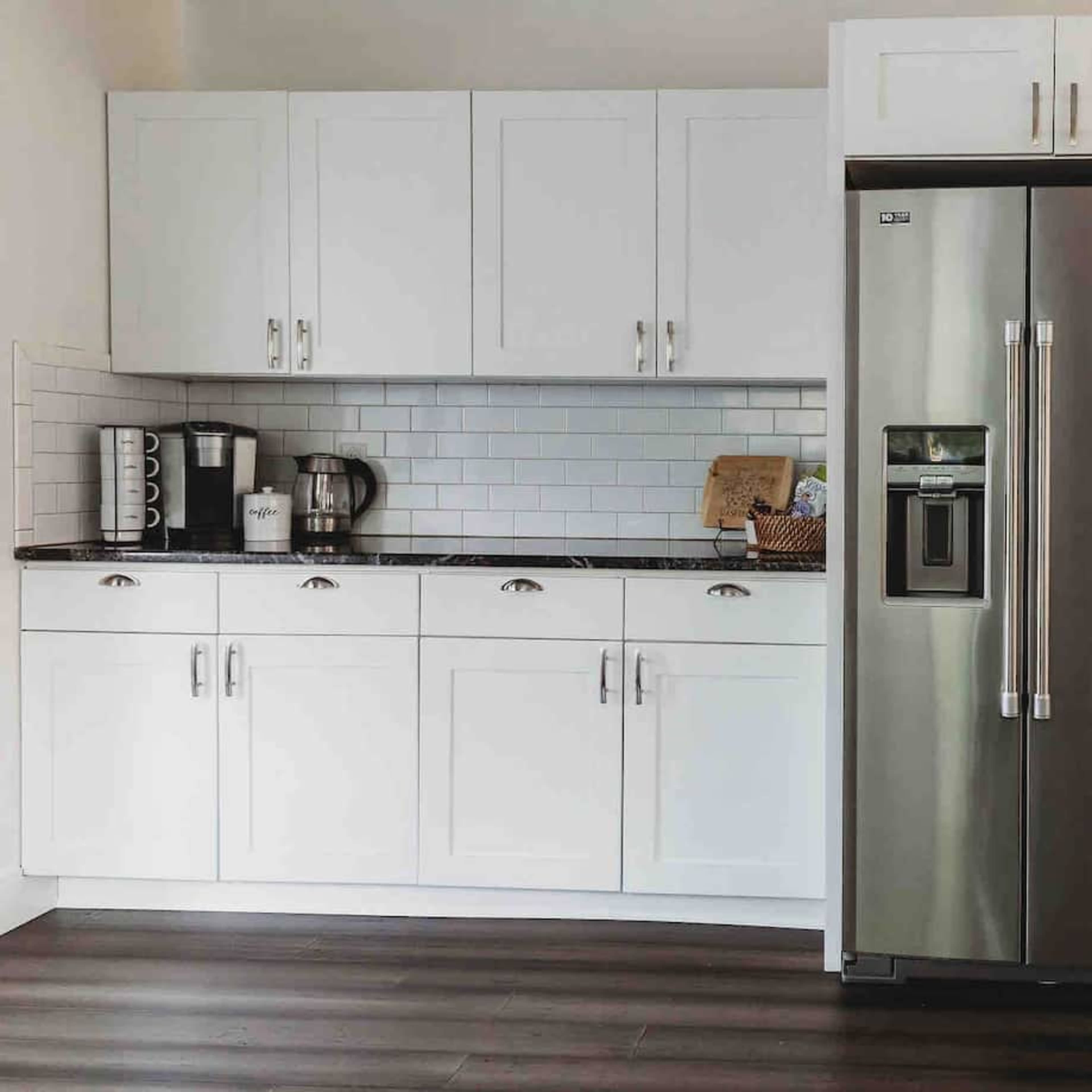 A modern kitchen area with a stainless steel refrigerator, white cabinetry, and a small workspace featuring a brown chair and a world map on the wall.