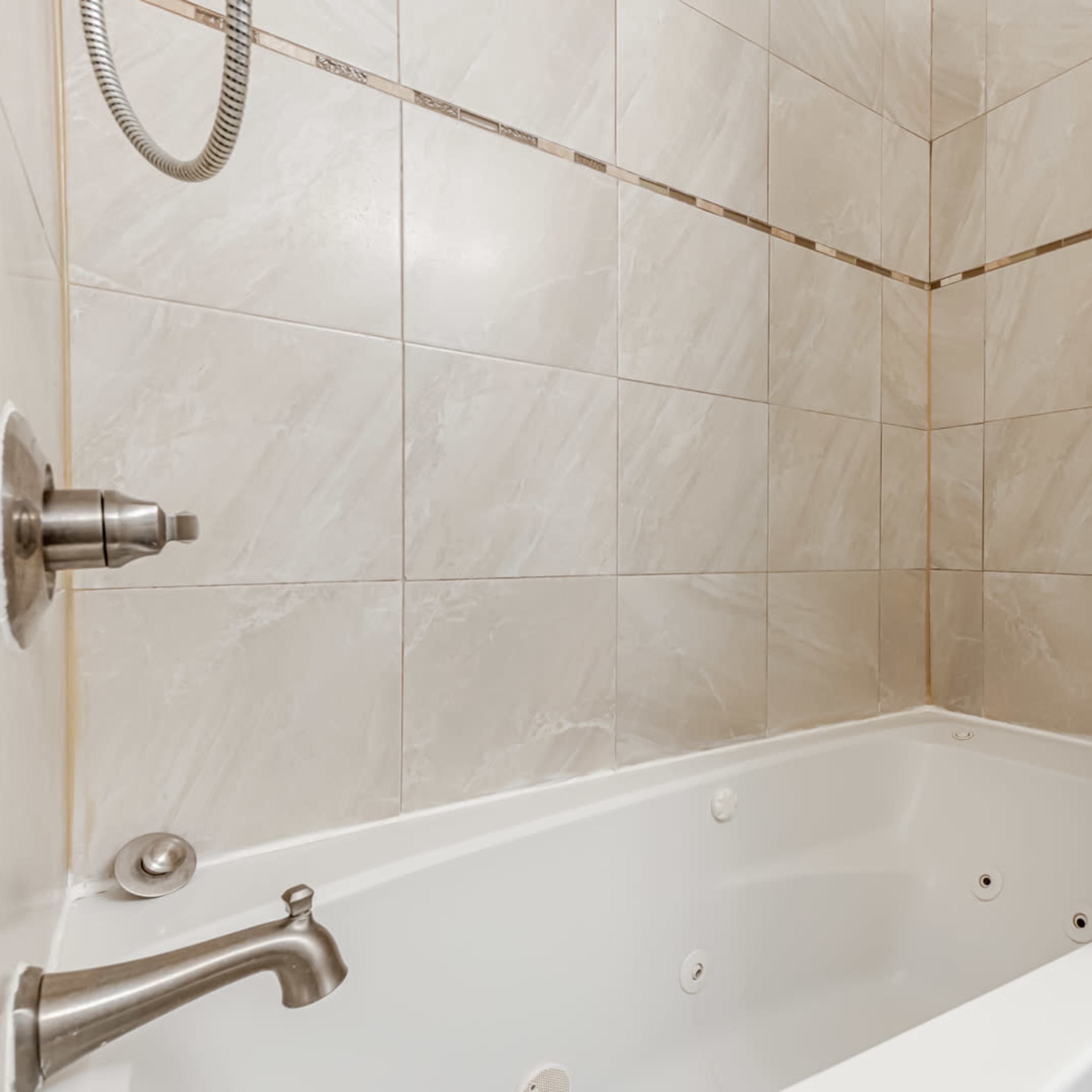 A corner of a bathroom featuring a tiled shower with a bathtub, a handheld showerhead, and a white shower curtain.