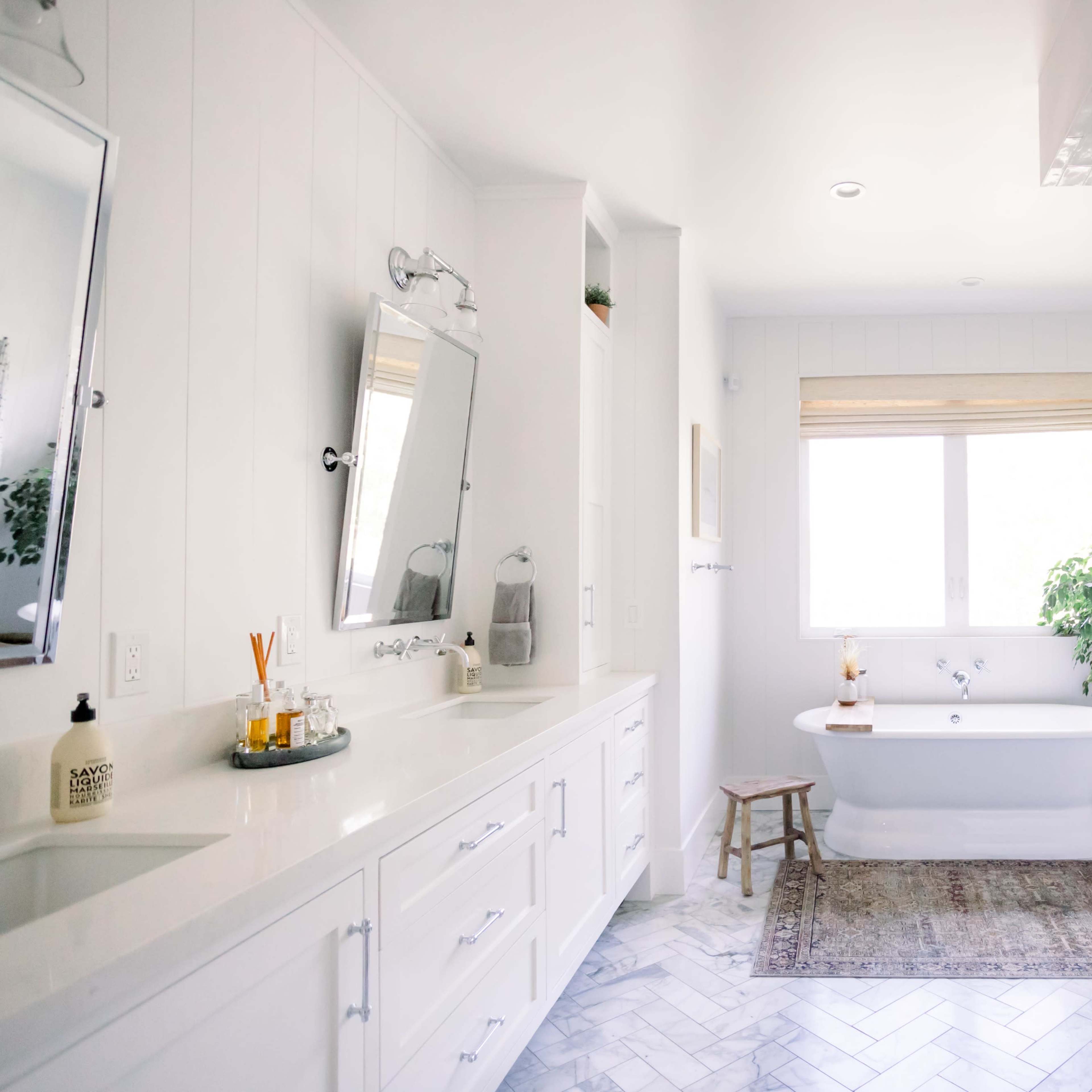 A bright, modern bathroom featuring a freestanding bathtub, a glass shower enclosure, and dual sinks with mirrors.