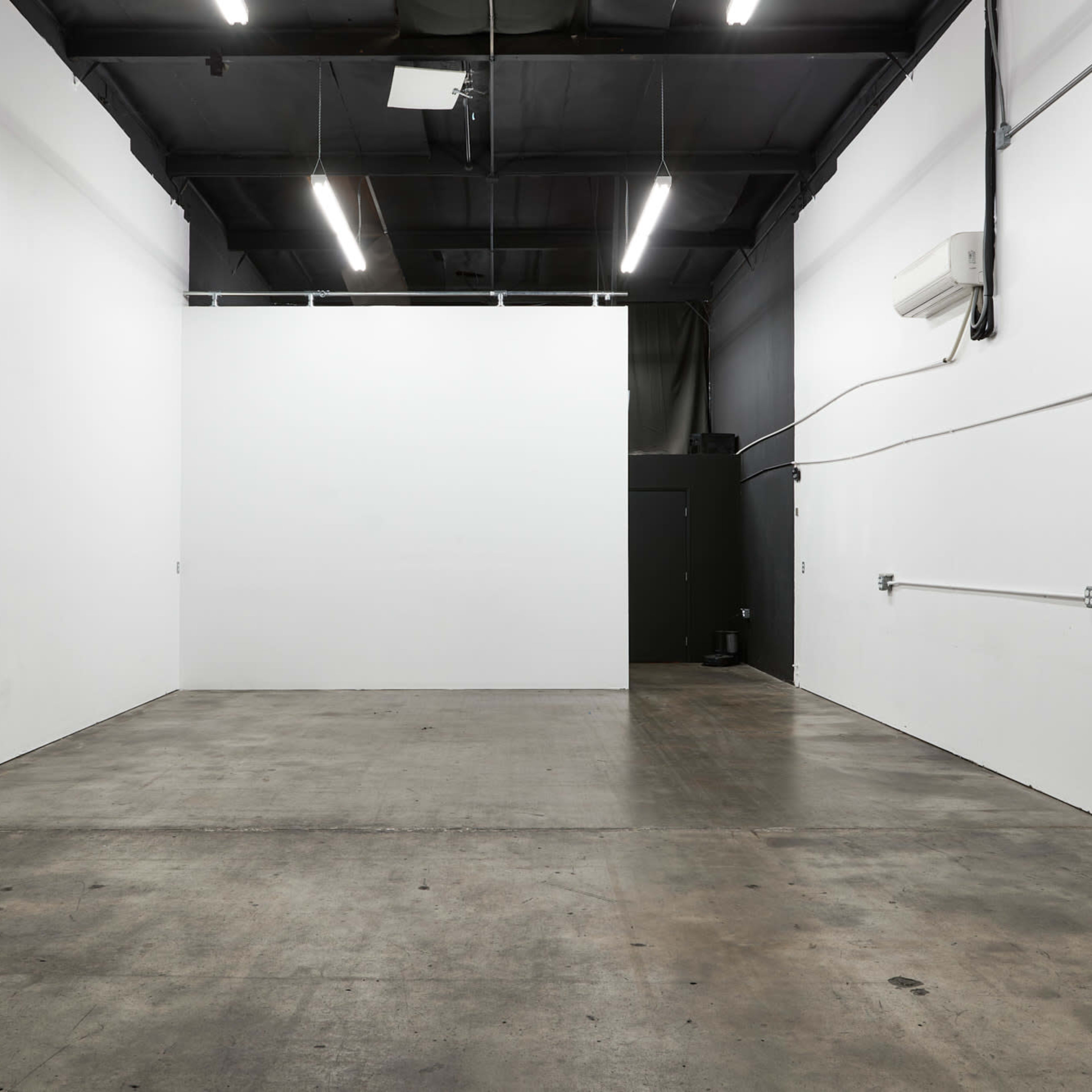 An empty room with concrete flooring, white walls, and overhead fluorescent lights.