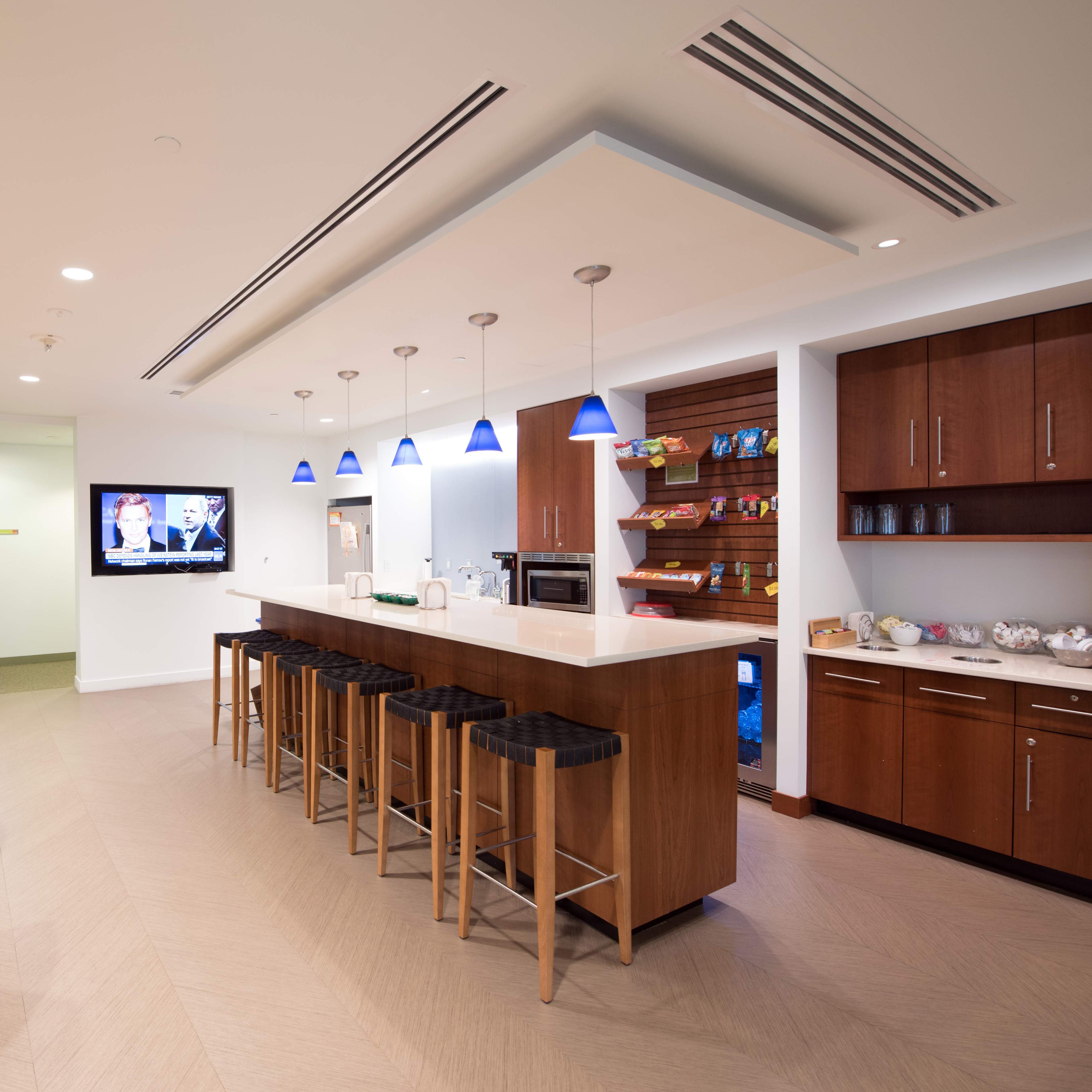 A modern kitchen and lounge area with a bar seating, a television on the wall, and various snacks displayed on shelves.