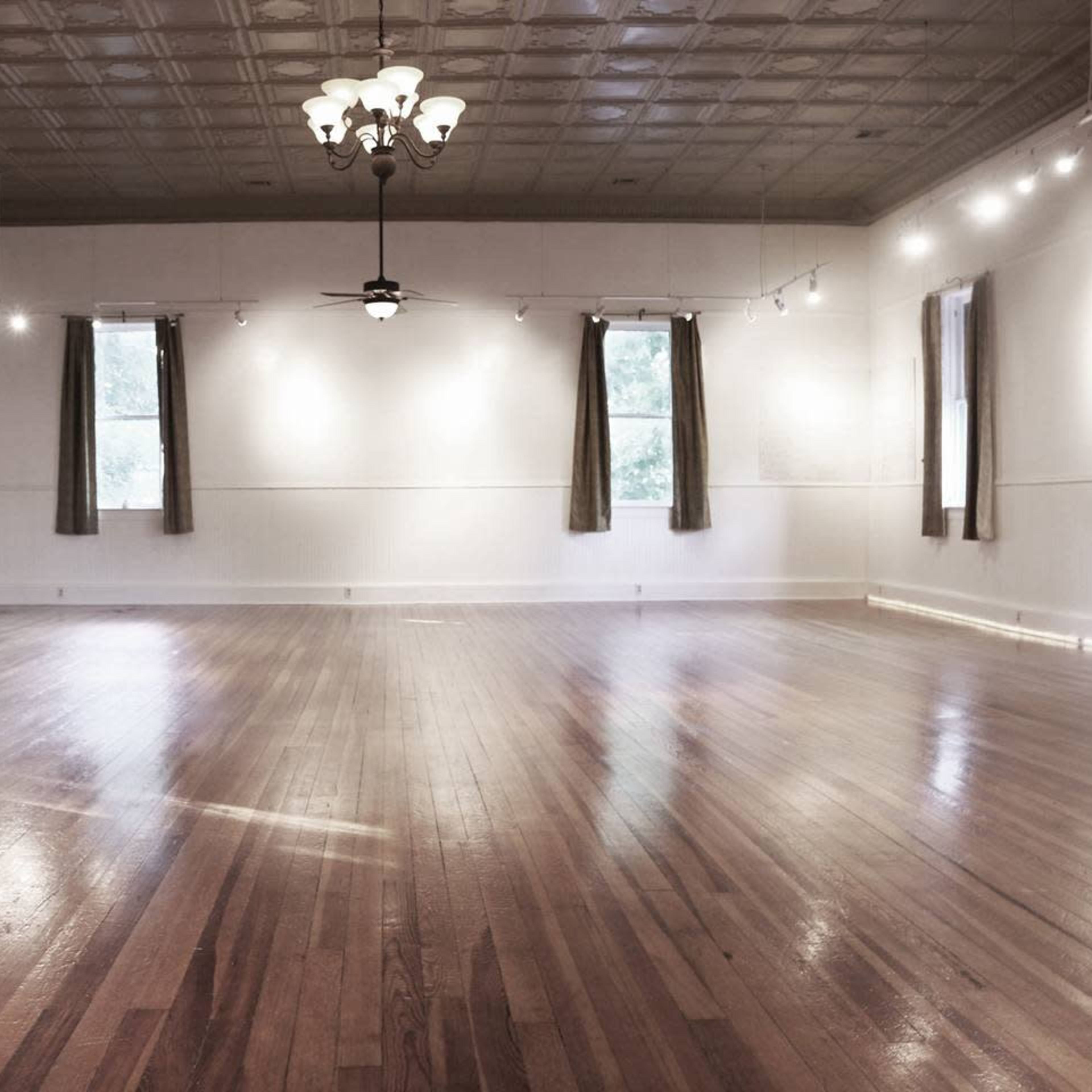 An empty room with hardwood floors, decorative lighting, and windows with curtains.