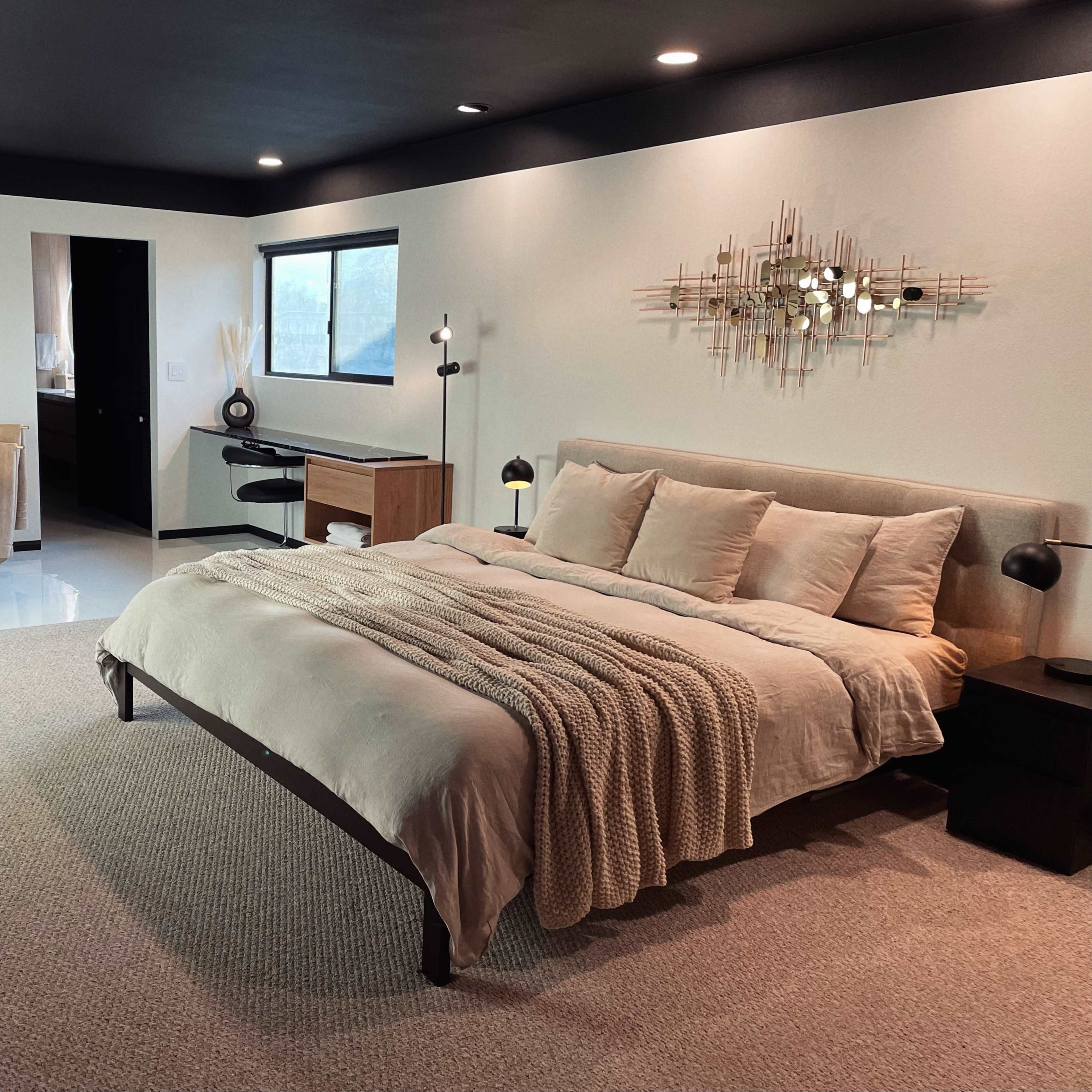 A modern bedroom featuring a large bed with neutral bedding, a freestanding tub, and minimalist decor with framed pictures on the walls.