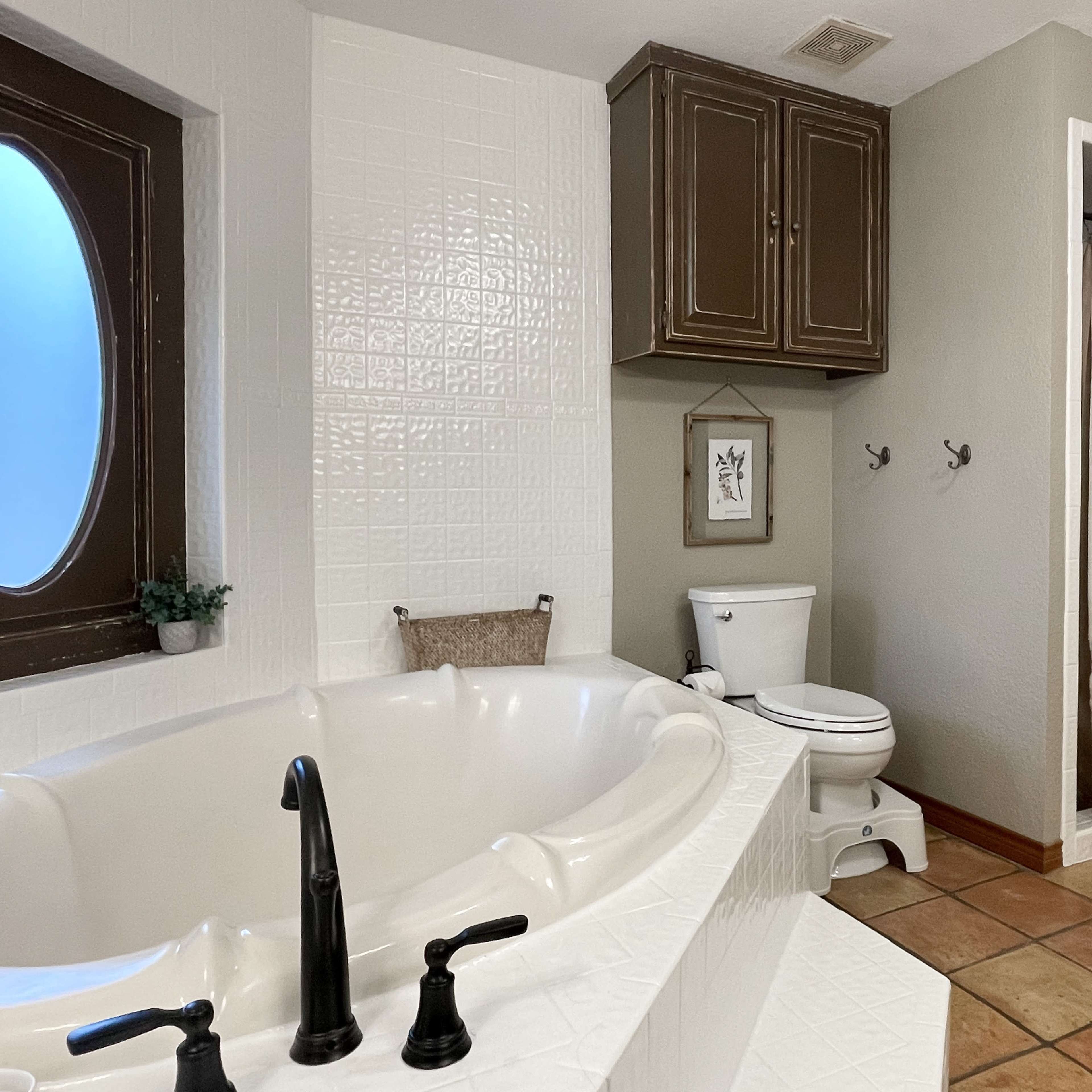 The bathroom features a large jetted tub, a toilet, a shower curtain, and tiled flooring.