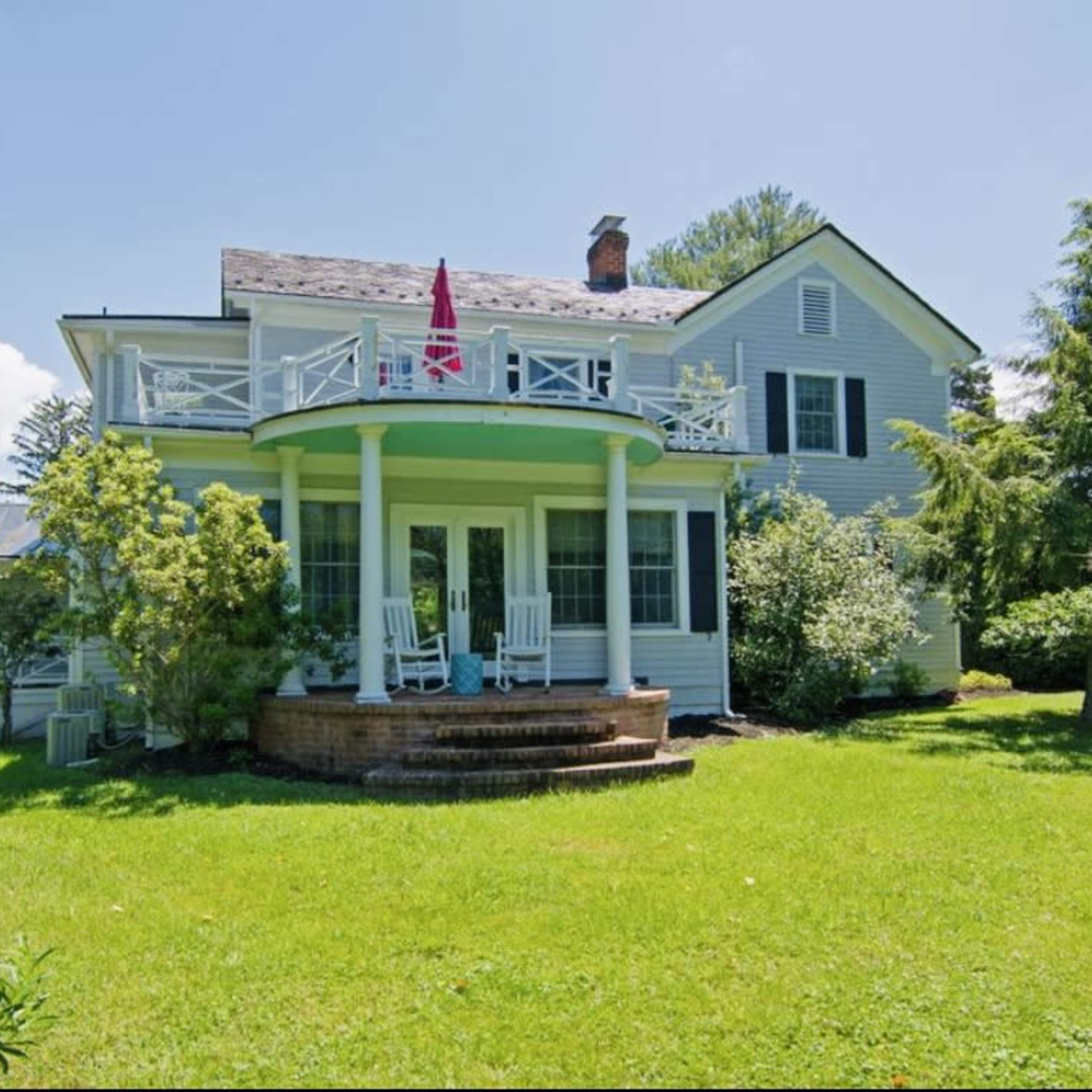 A large, two-story house with a curved porch, surrounded by green lawn and trees.