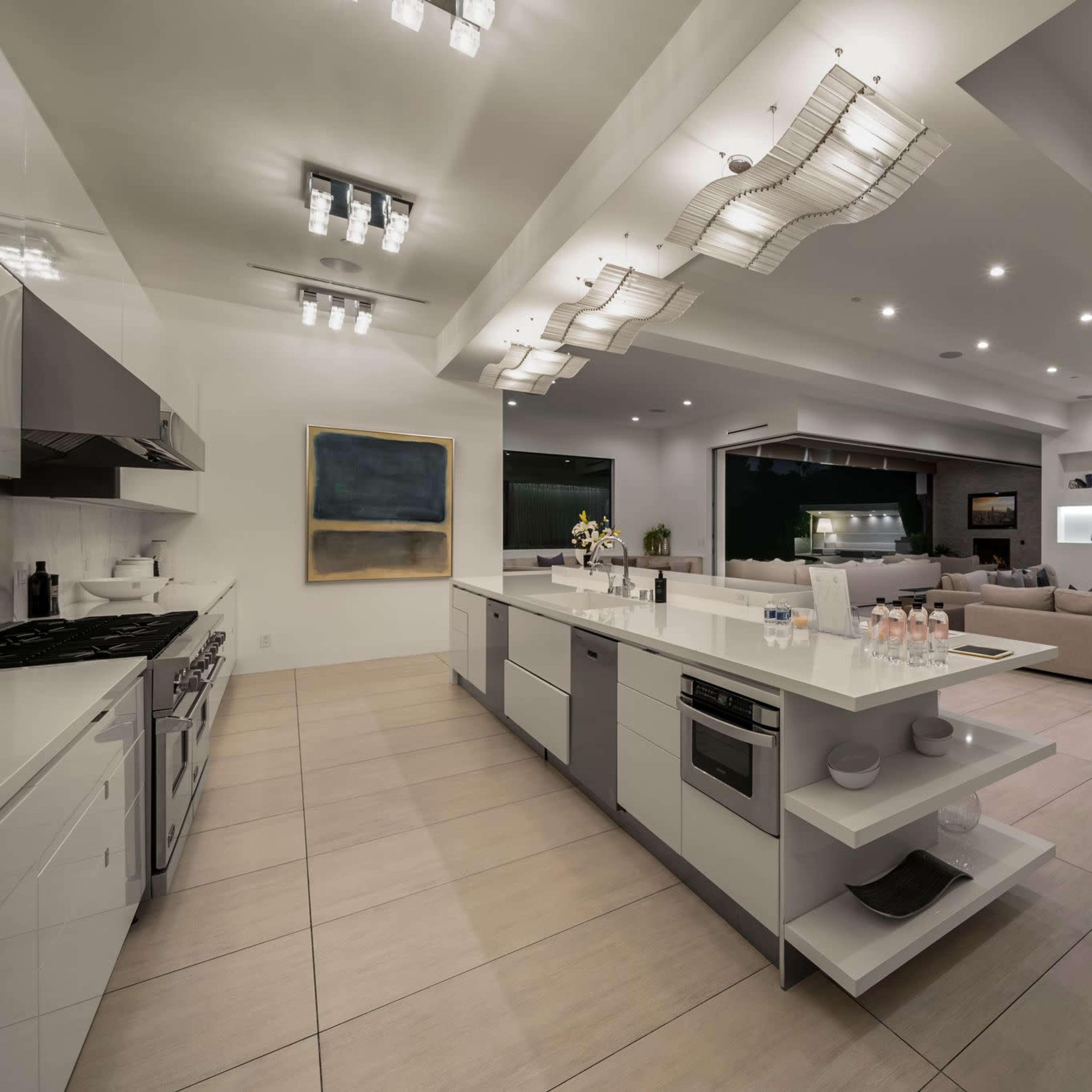 A modern, open-concept kitchen and living area with sleek, white cabinetry, a central island, and a spacious seating arrangement.