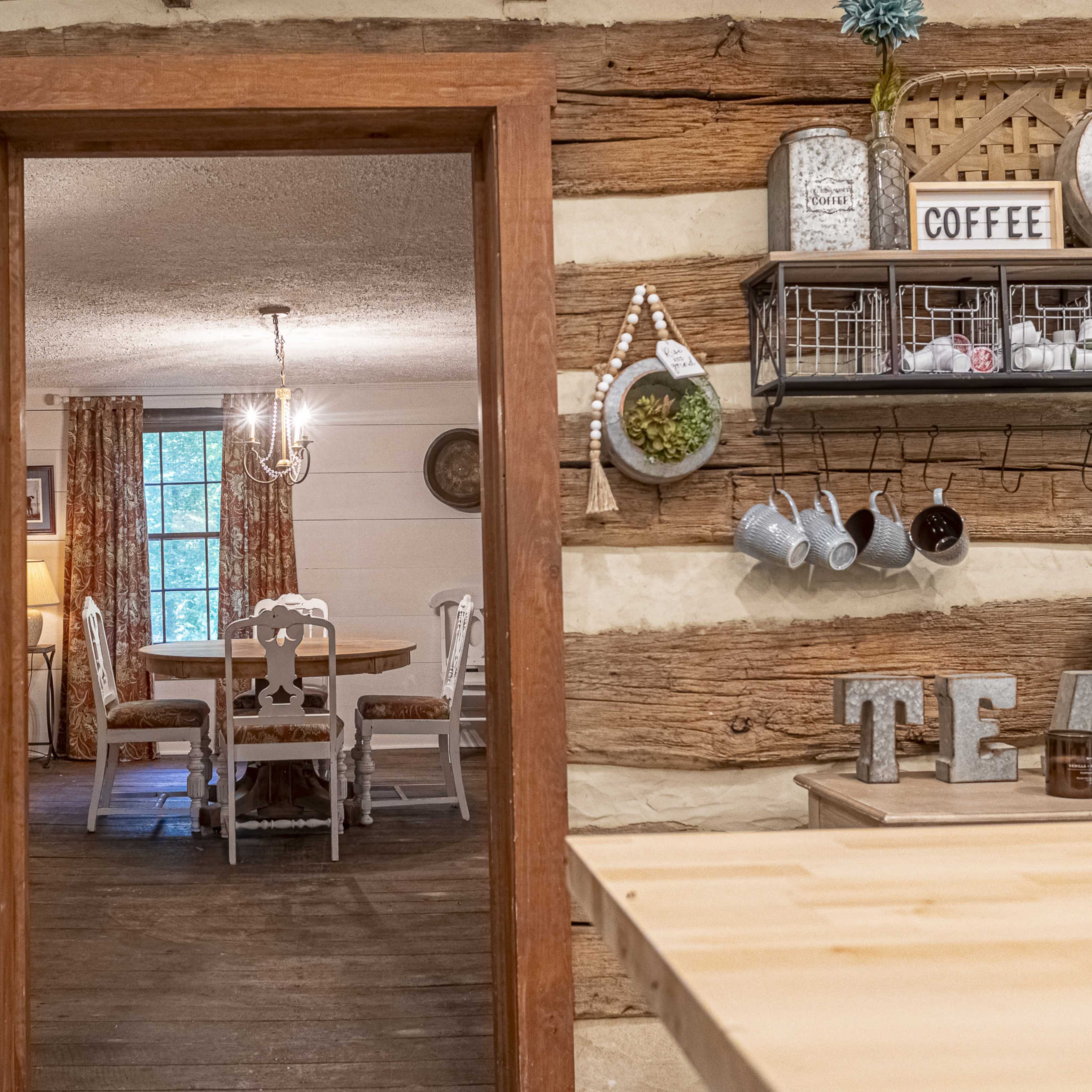 A wooden interior with a doorway leading to a dining area furnished with a round table and chairs, surrounded by rustic decor.