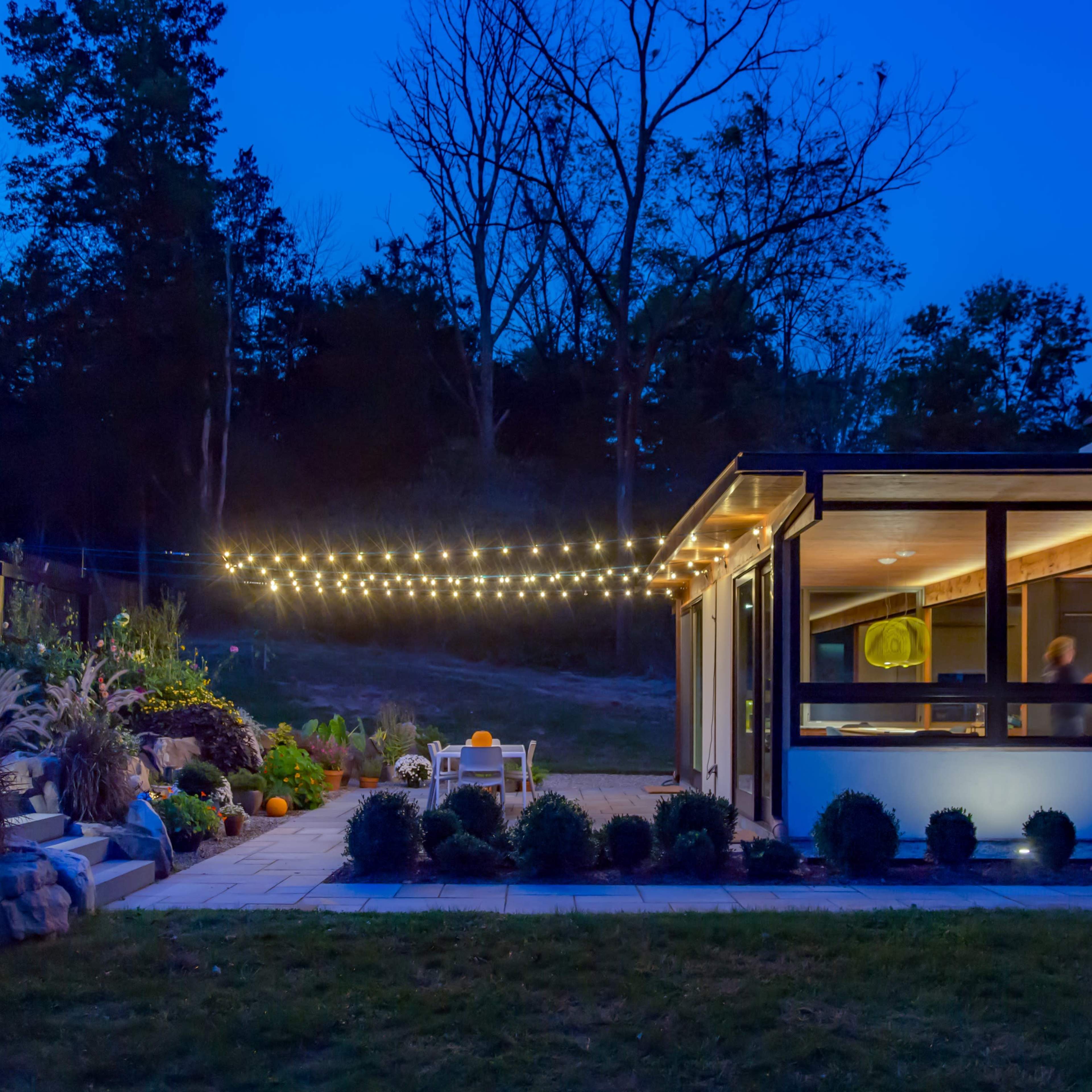 A modern house with outdoor string lights and a landscaped yard is set against a twilight sky.