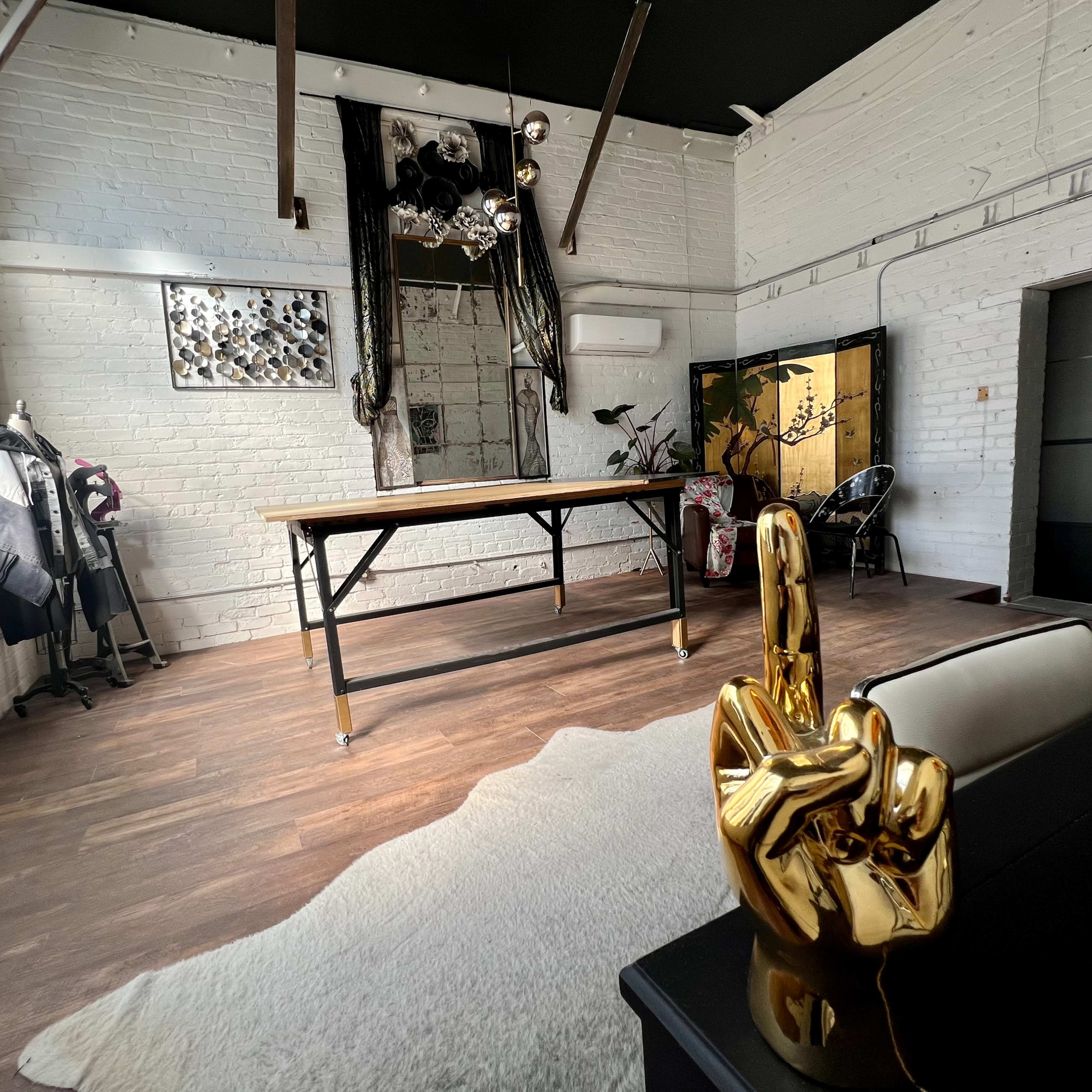 A spacious, brightly lit interior featuring a large wooden table, decorative sculptures, and a mix of furniture against a backdrop of white brick walls.