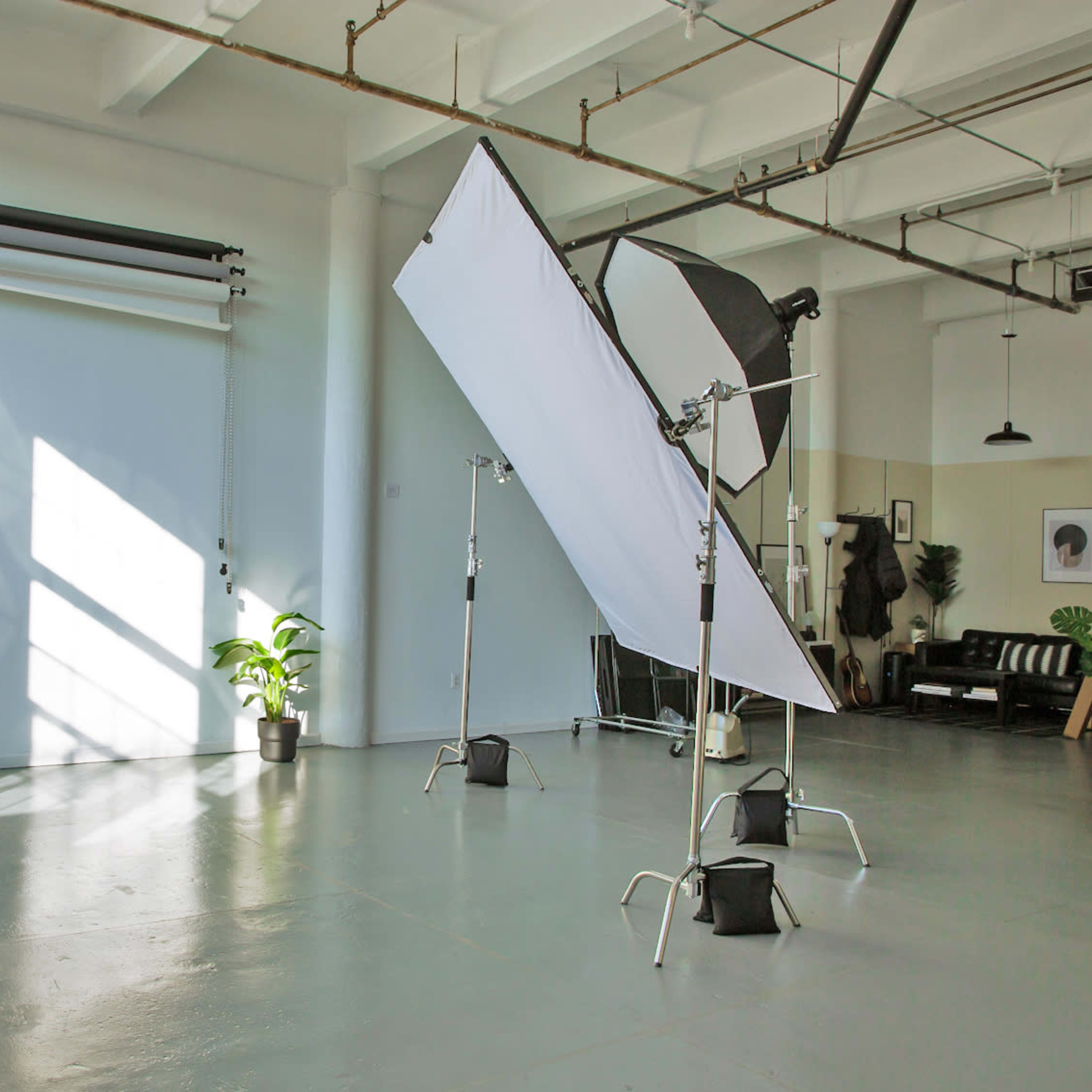A bright photography studio with large windows, a backdrop on the left, and lighting equipment set up in the center.