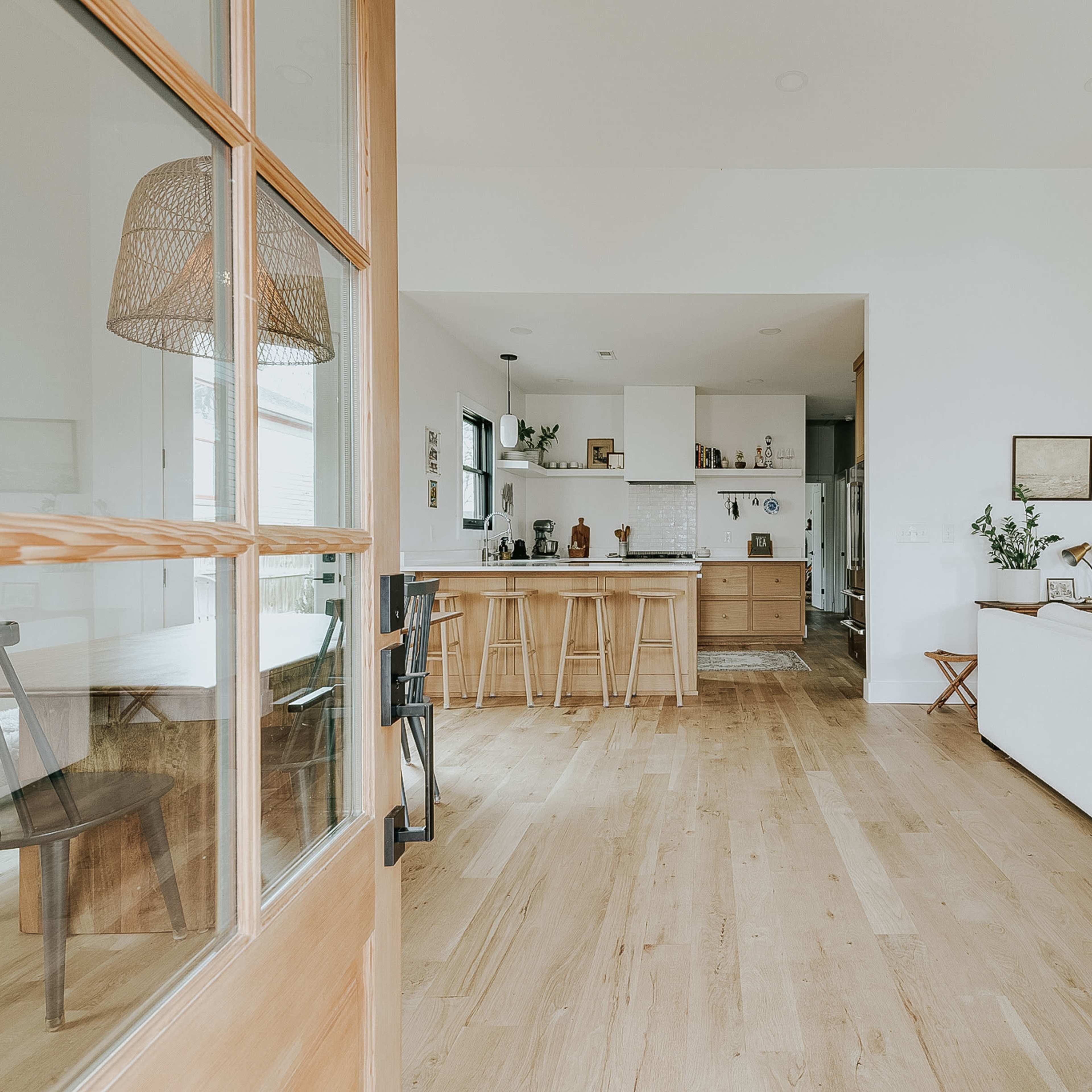 A welcoming interior features a bright open space with a modern kitchen, wooden flooring, and a brick accent wall.